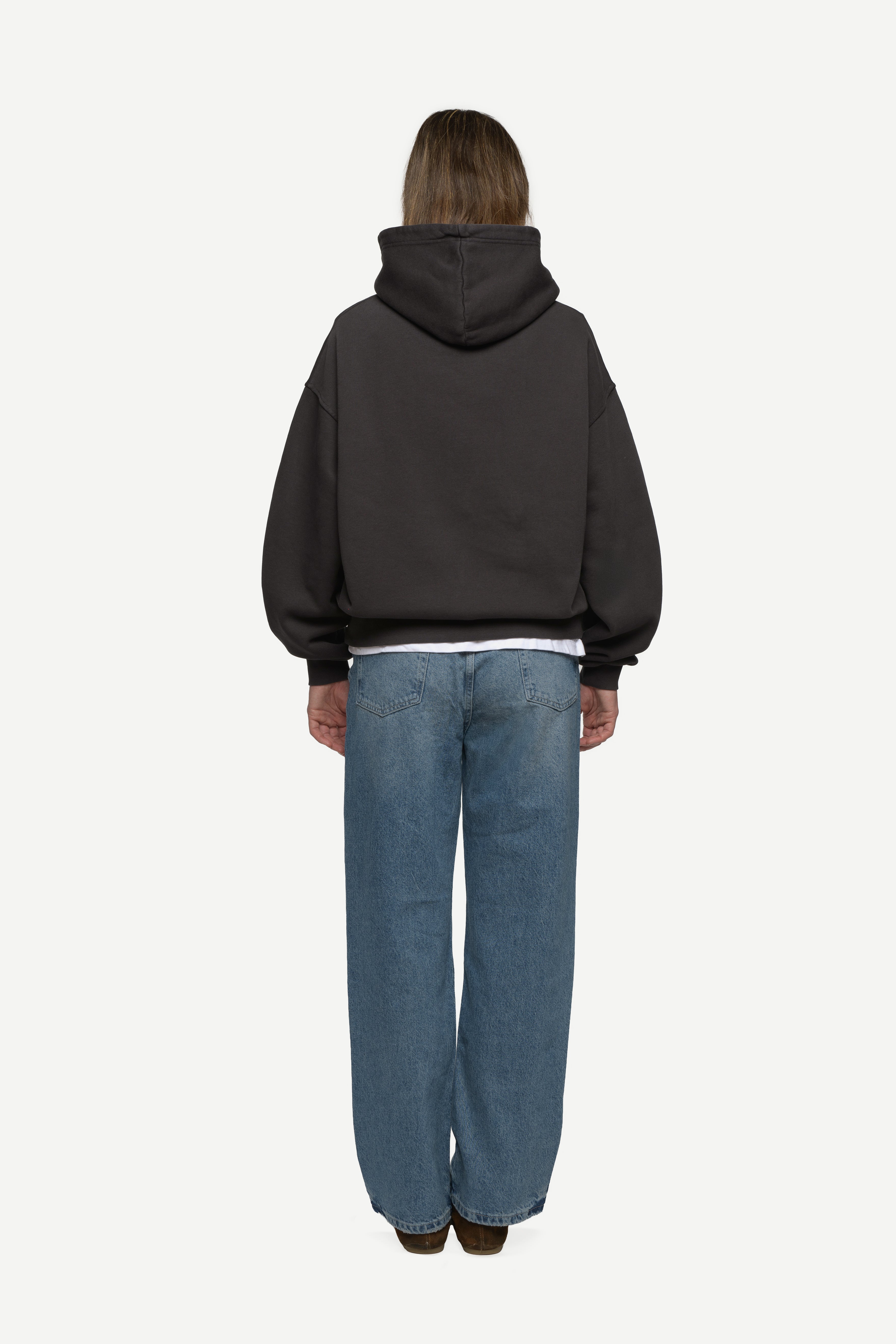 back view of woman wearing a black hoodie and blue jeans on a white background