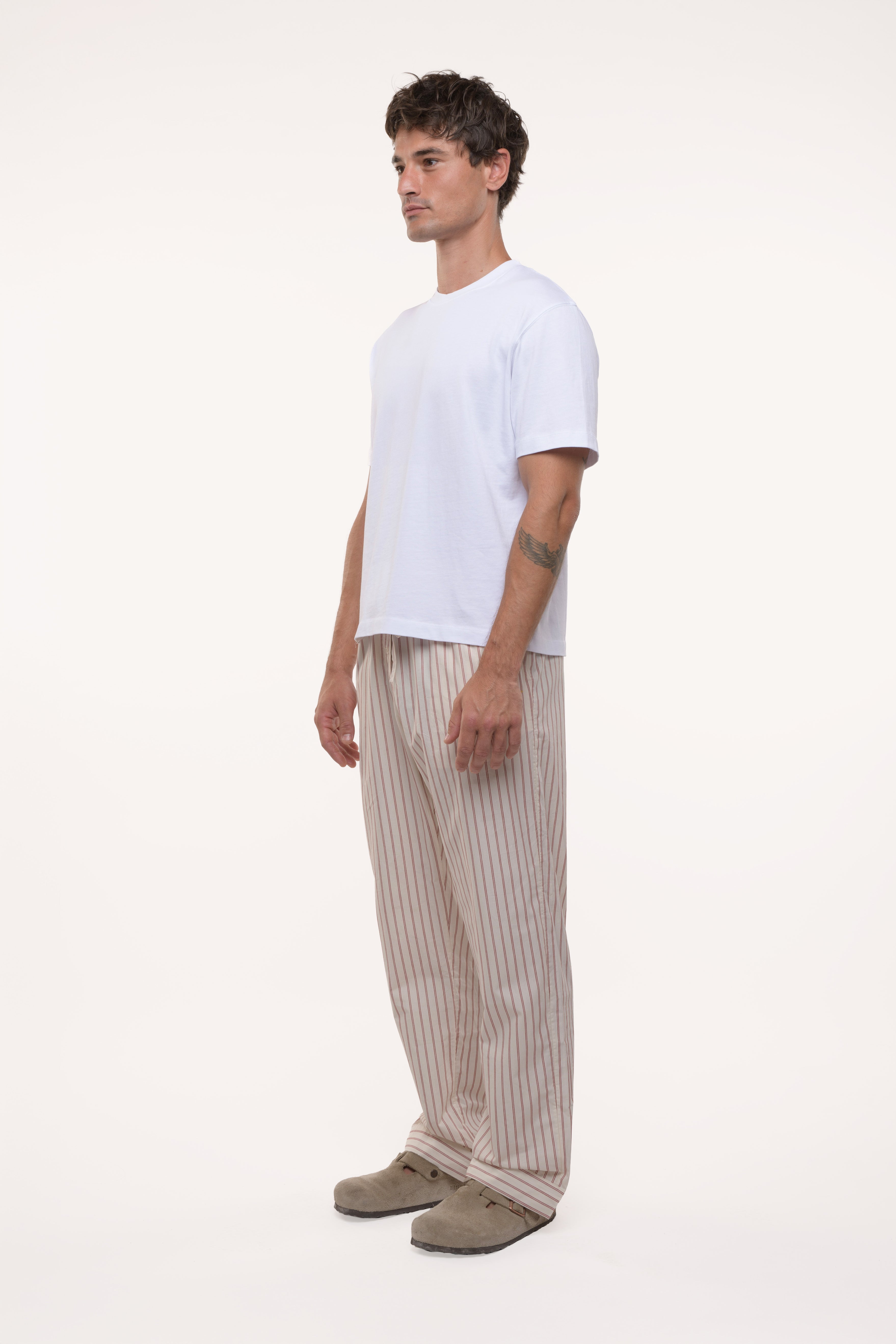 Side view of a man wearing a white t-shirt and beige striped pants on a white background