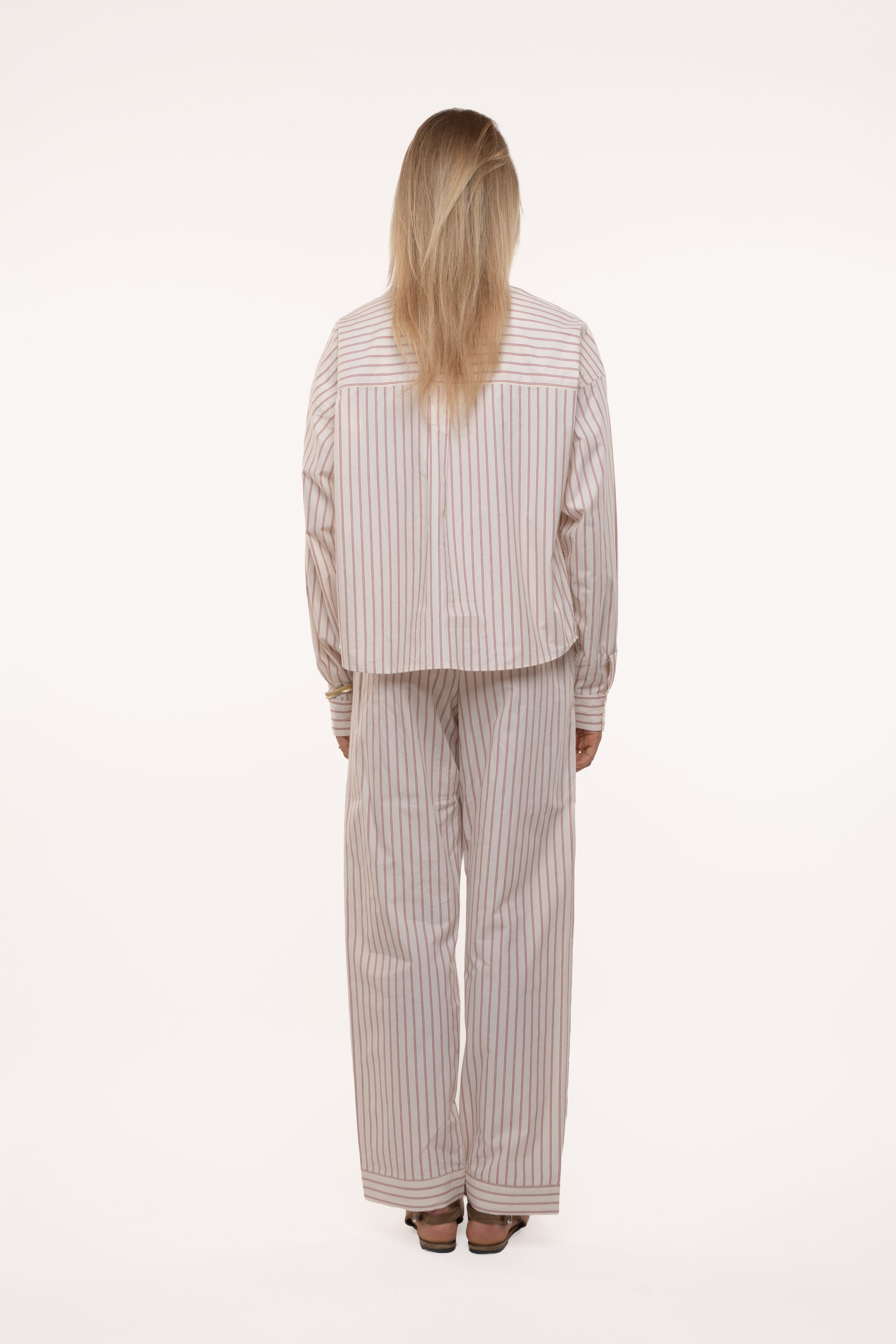 Back view of a woman wearing a beige striped outfit on a white background