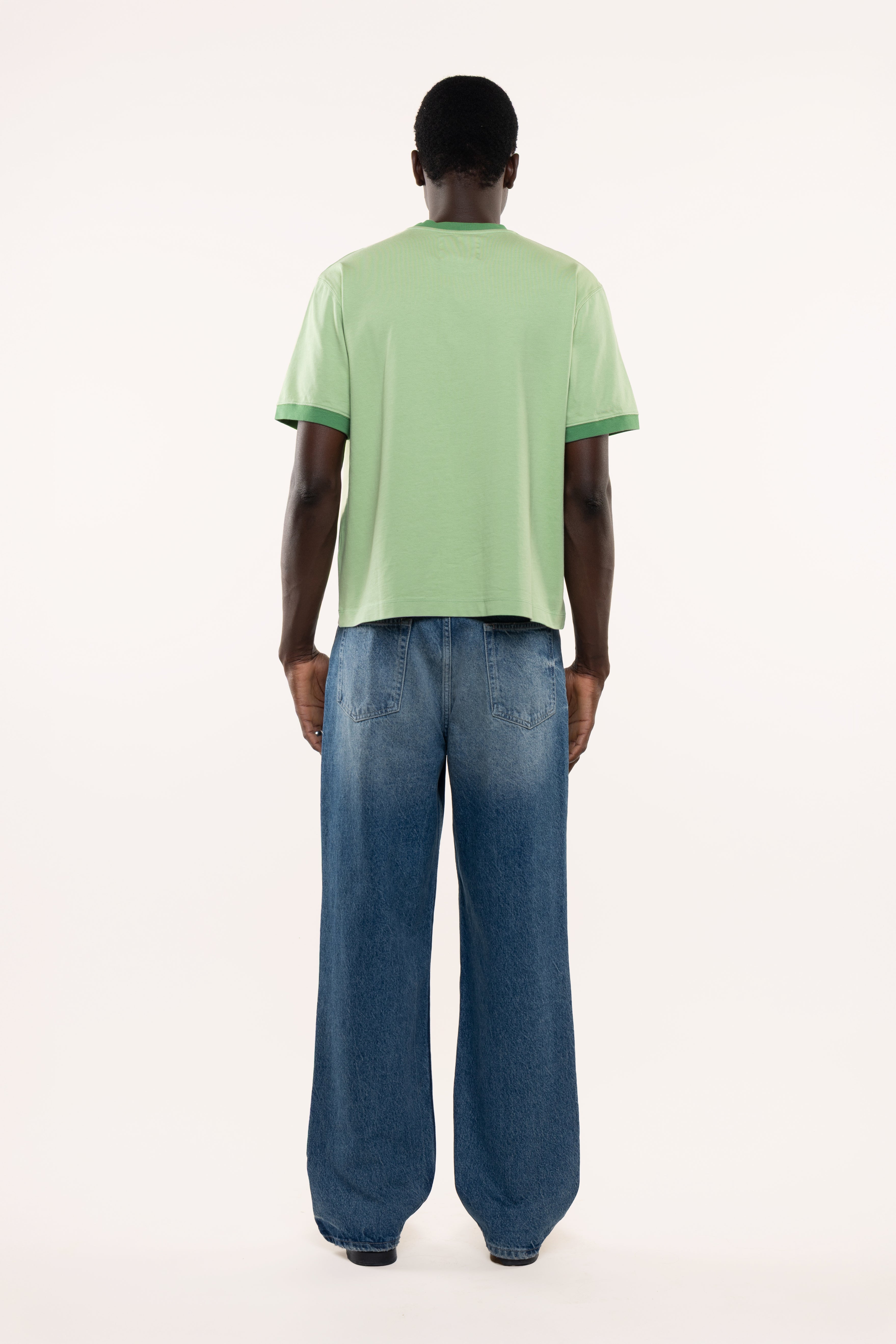 Back view of a man wearing a light green t-shirt and blue jeans on a white background