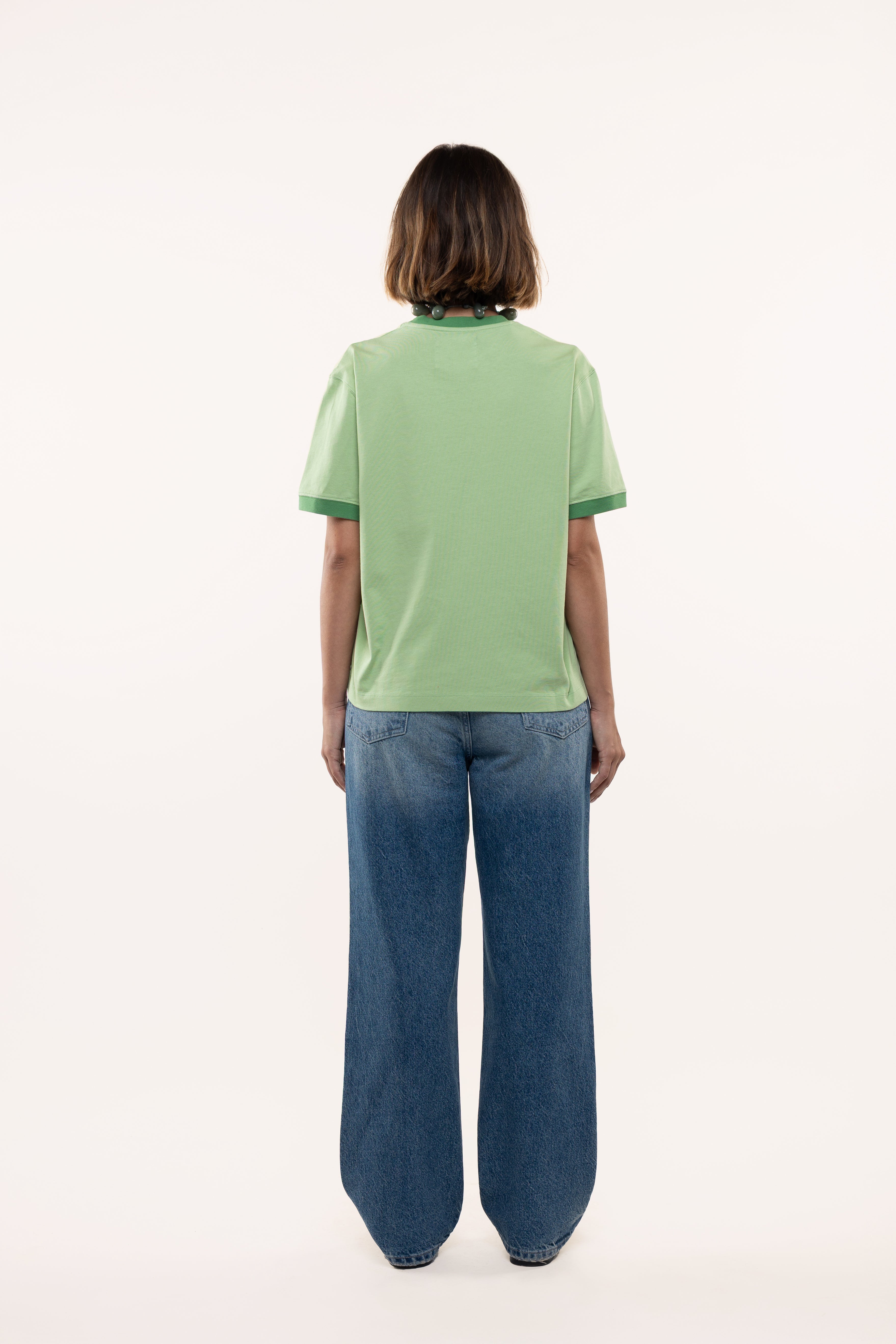 Back view of a woman wearing a green t-shirt and blue jeans on a white background