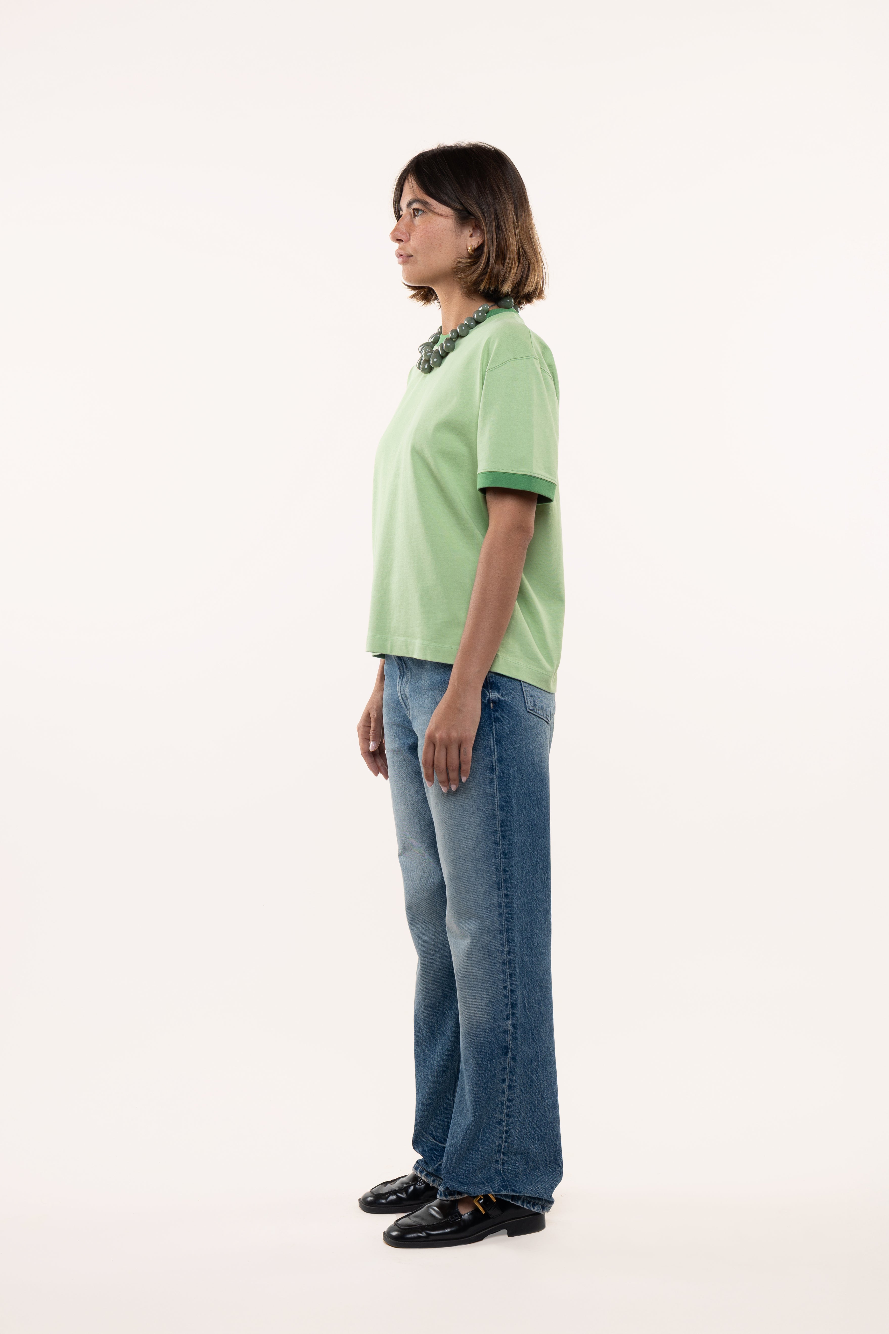 Side view of a woman wearing a green shirt and blue jeans on a white background