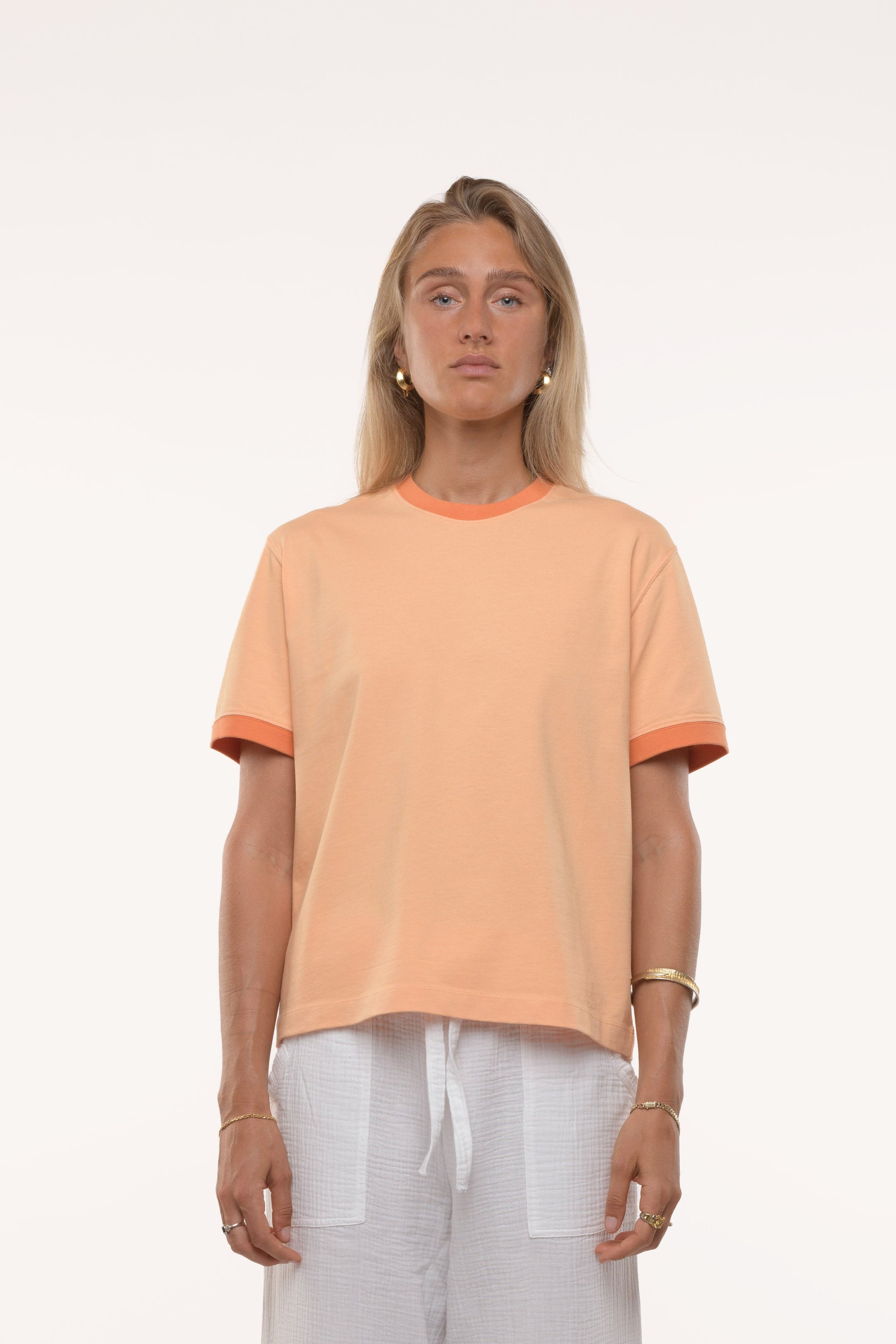 Woman wearing a peach-colored t-shirt and white pants on a white background