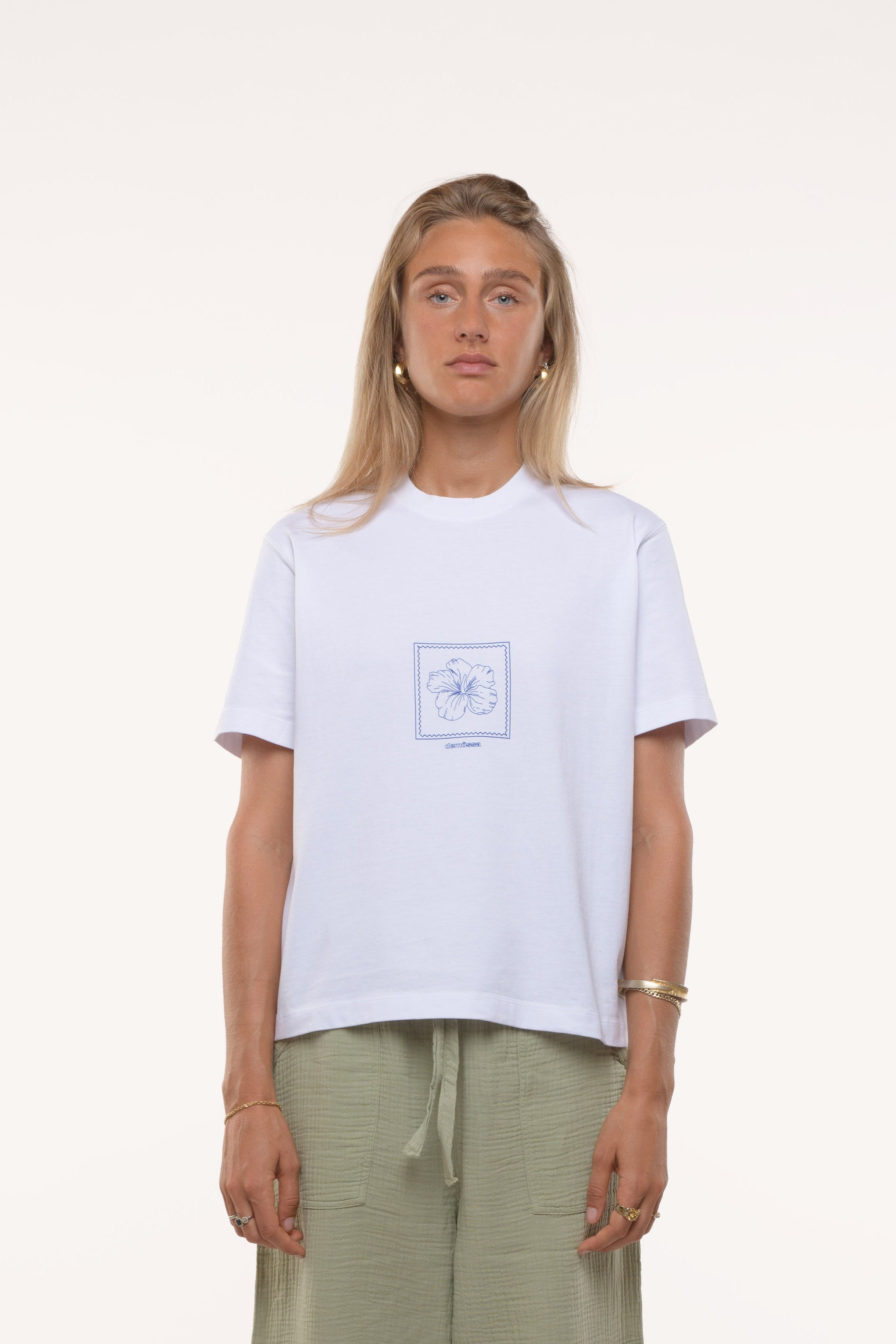 Woman wearing a white t-shirt with a flower graphic and light green pants on a white background