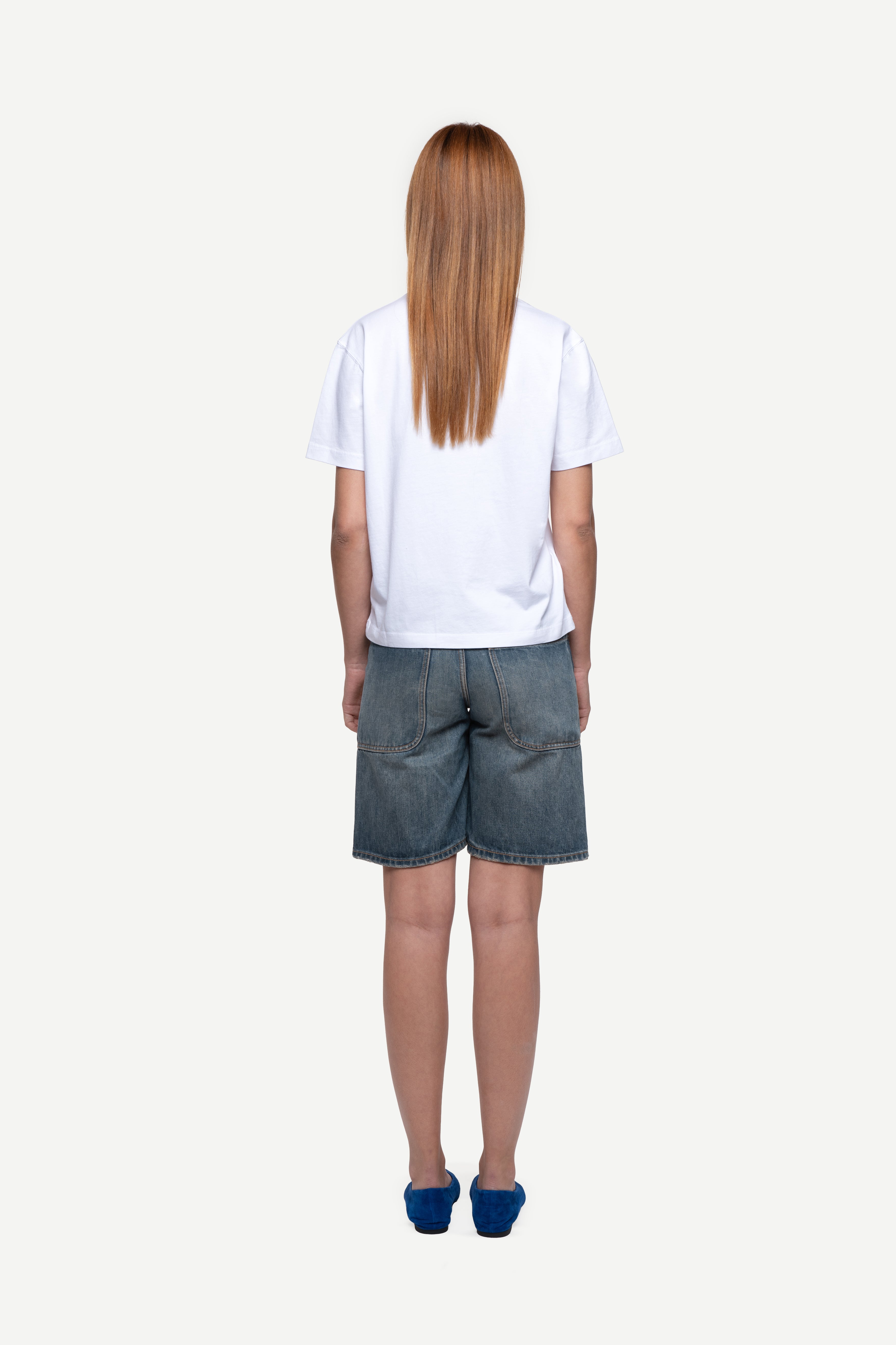 back view of woman wearing a regular fit black short-sleeved t-shirt, blue jeans and flip flops on a white background