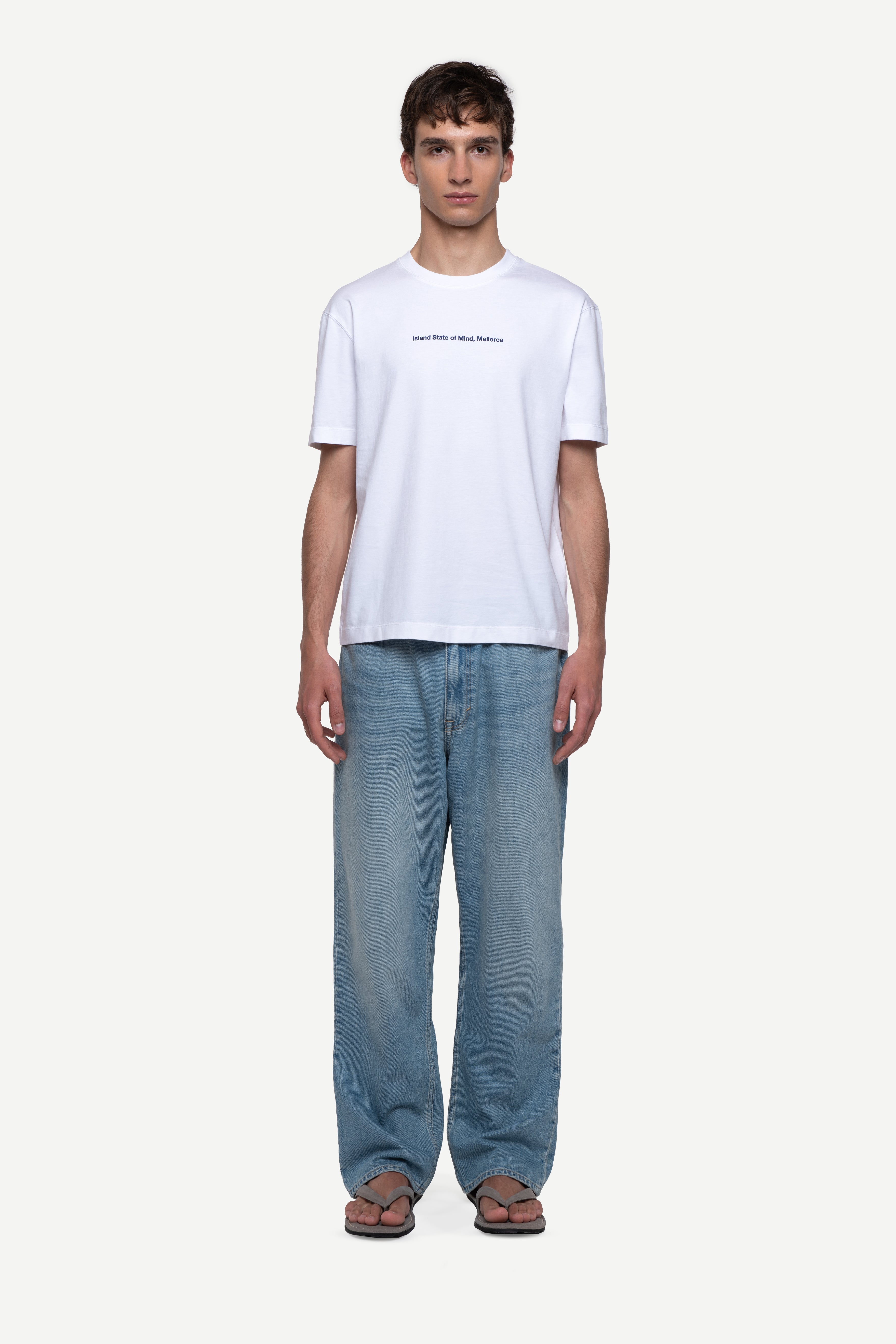 front view of man wearing a regular fit black short-sleeved t-shirt with white double-layered neckline, sleeves and hem, blue jeans and flip flops on a white background