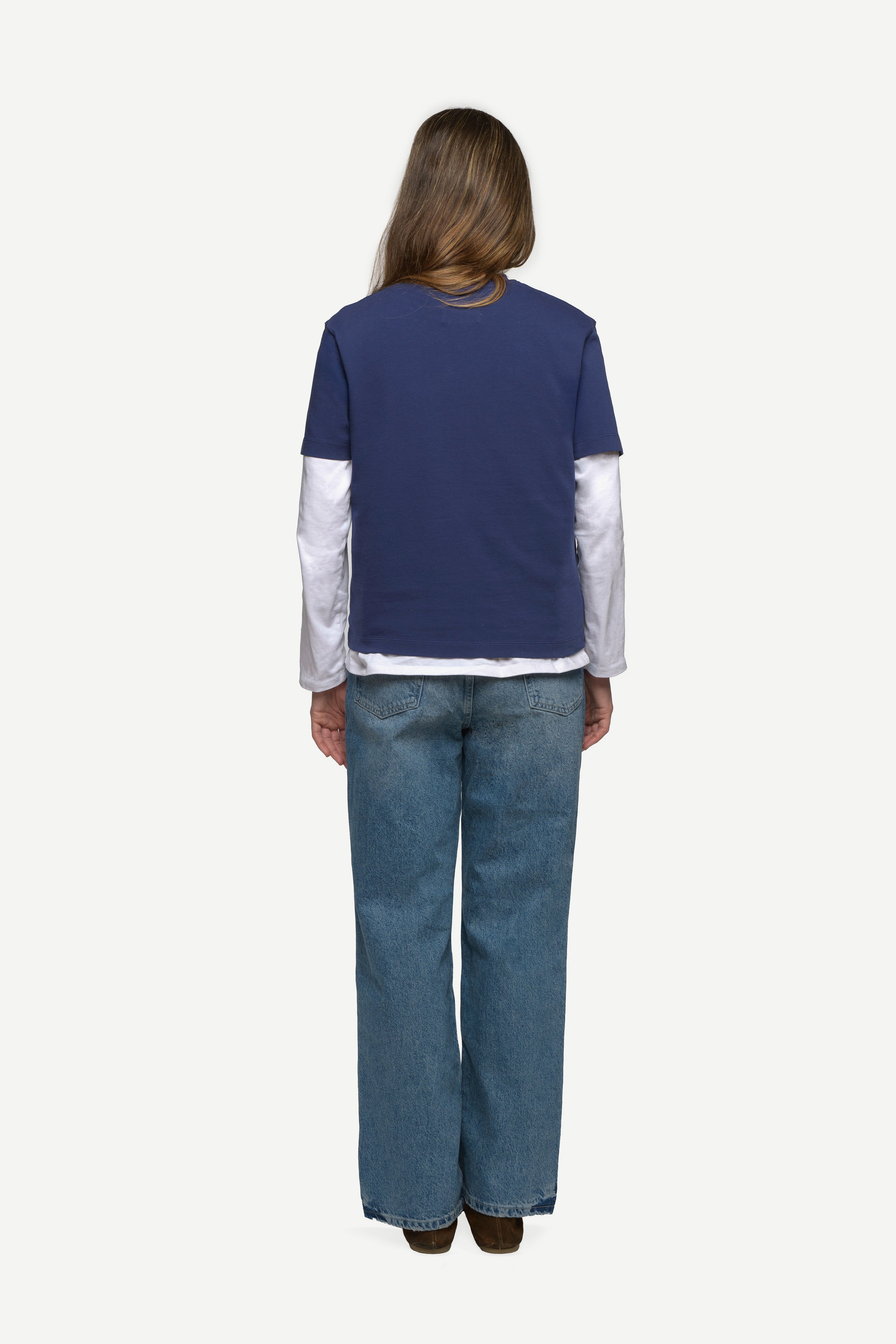 back view of woman wearing a navy t-shirt and blue jeans on a white background