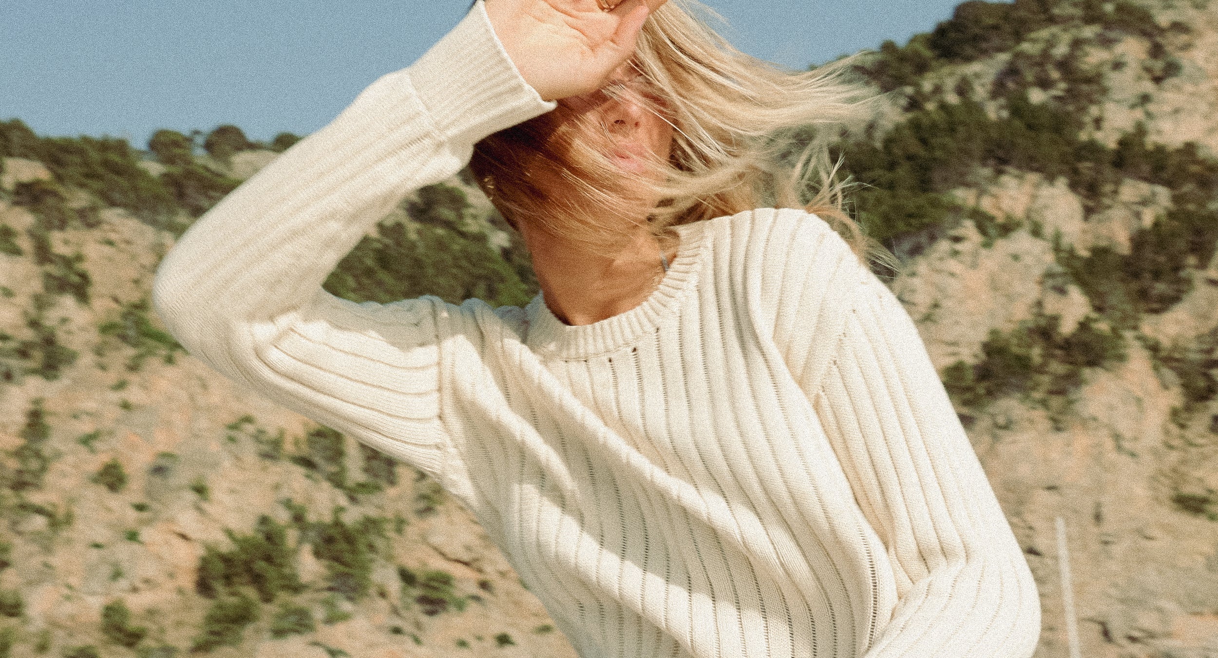 Person wearing a beige sweater with a mountainous landscape in the background