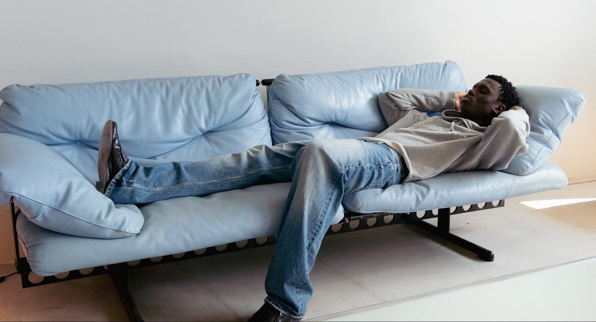 Person lying on a light blue sofa in a minimalistic room.