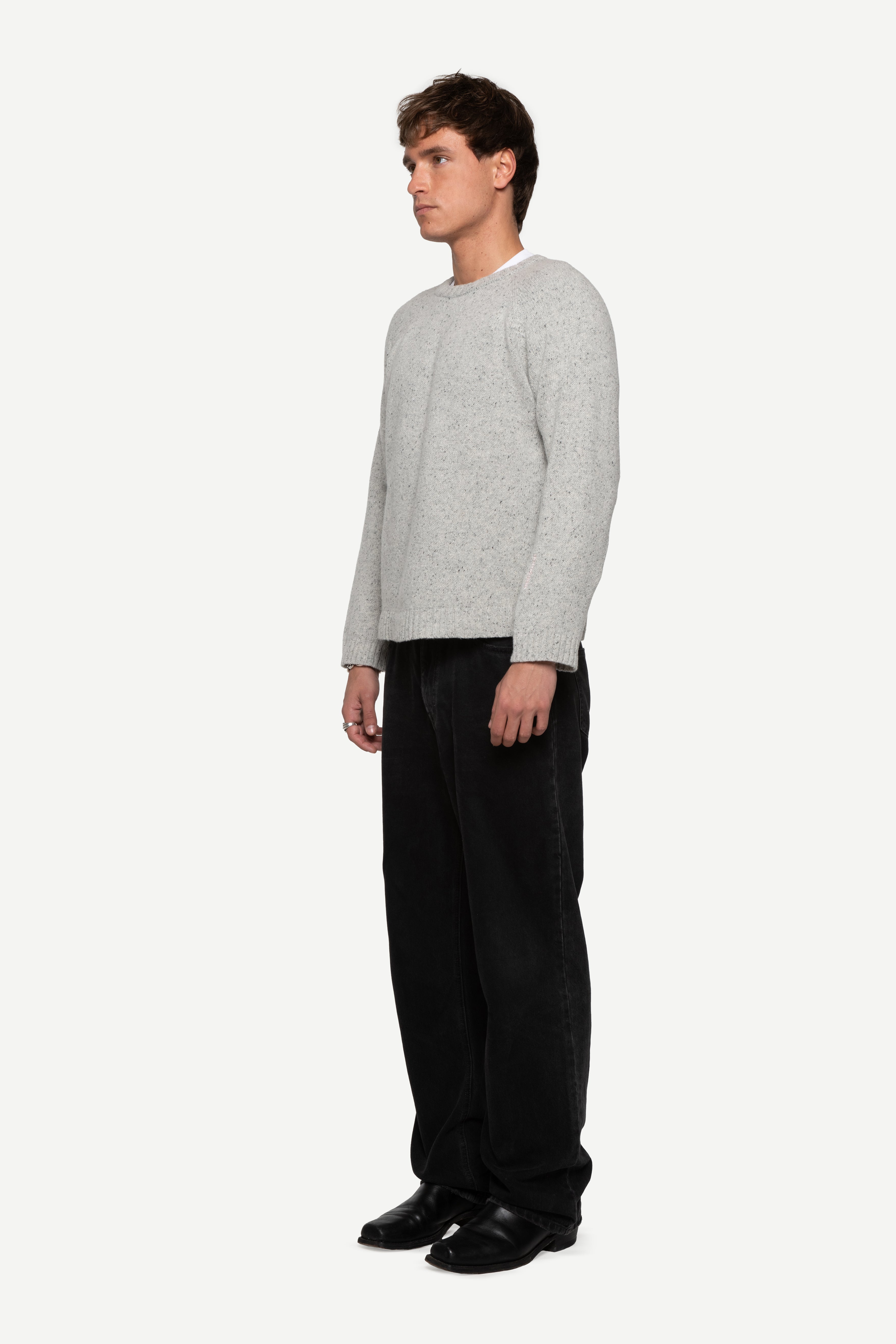 side view of man wearing a grey sweater made from a soft blend of wool and silk with black jeans on a white background