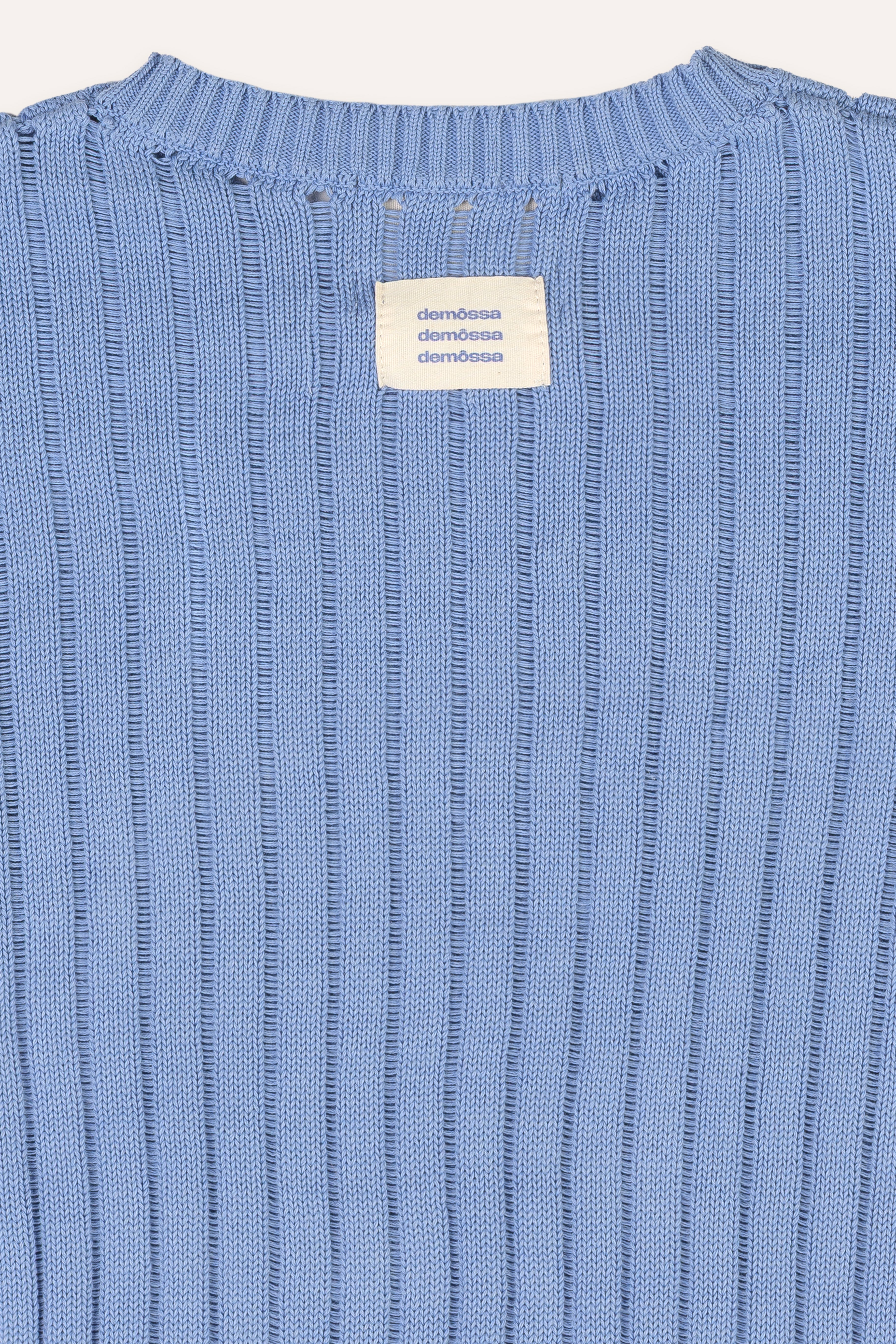 Close-up of a blue ribbed sweater with a brand label on a white background