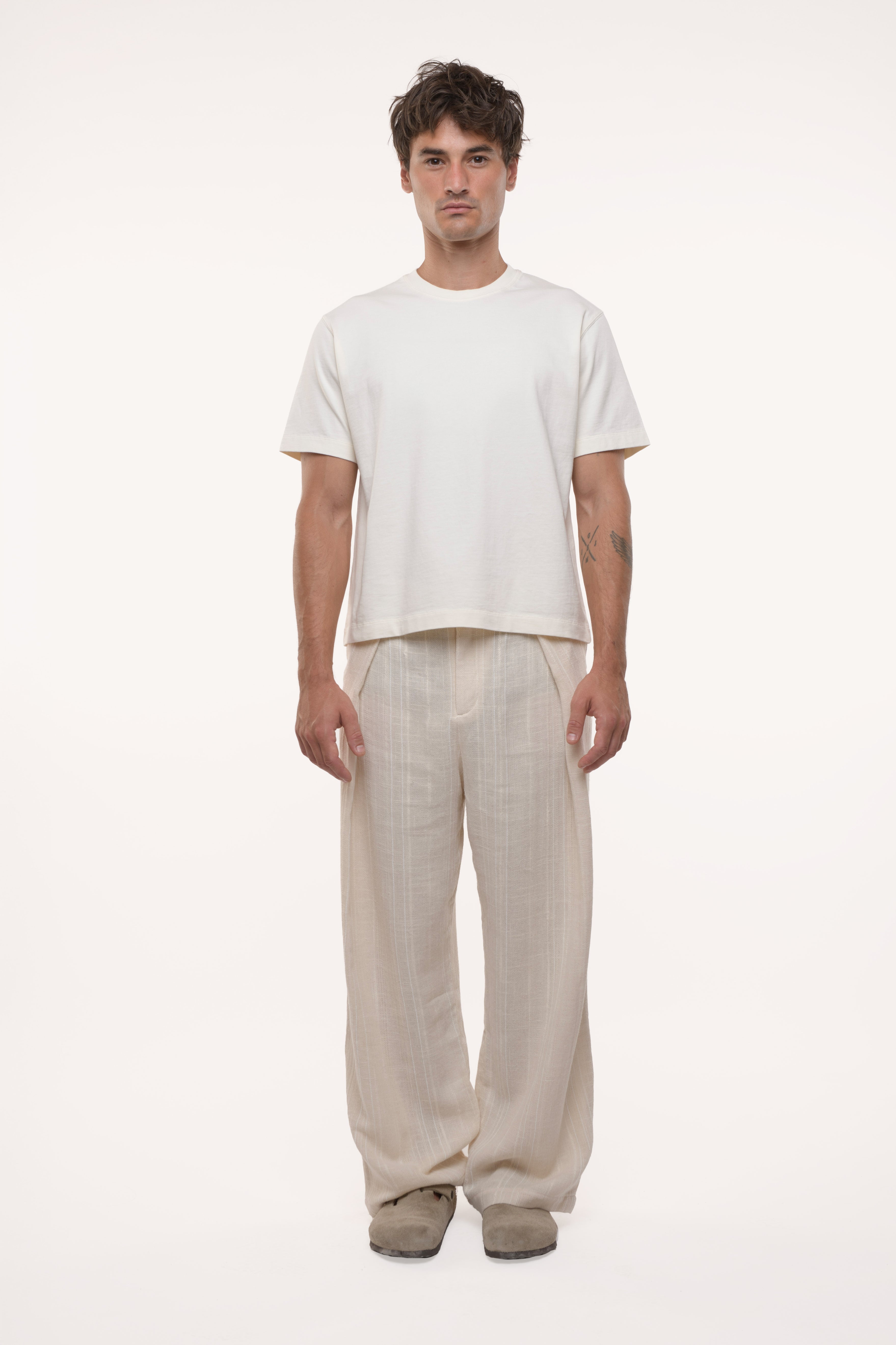Man wearing a white t-shirt and beige pleated pants on a white background