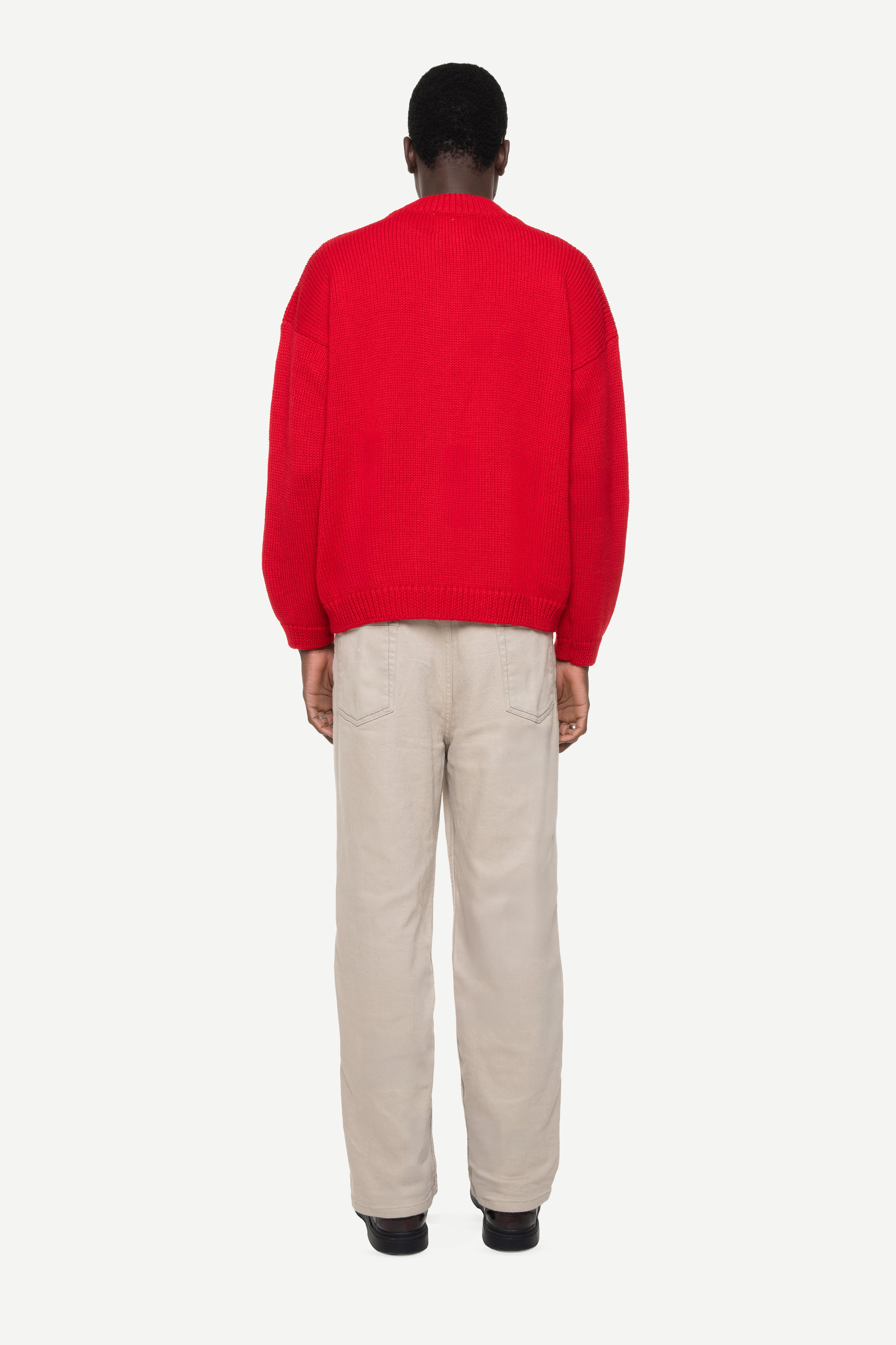 back view of a man wearing a red cardigan and beige jeans on a white background
