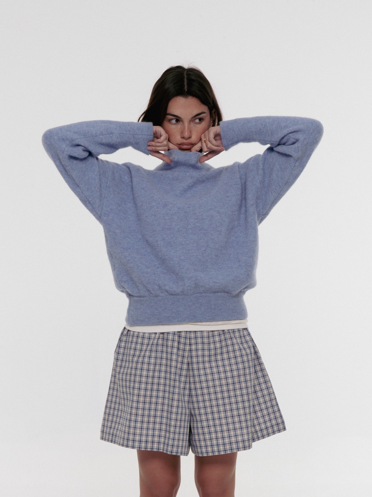 Person wearing a blue sweater and plaid shorts on a white background