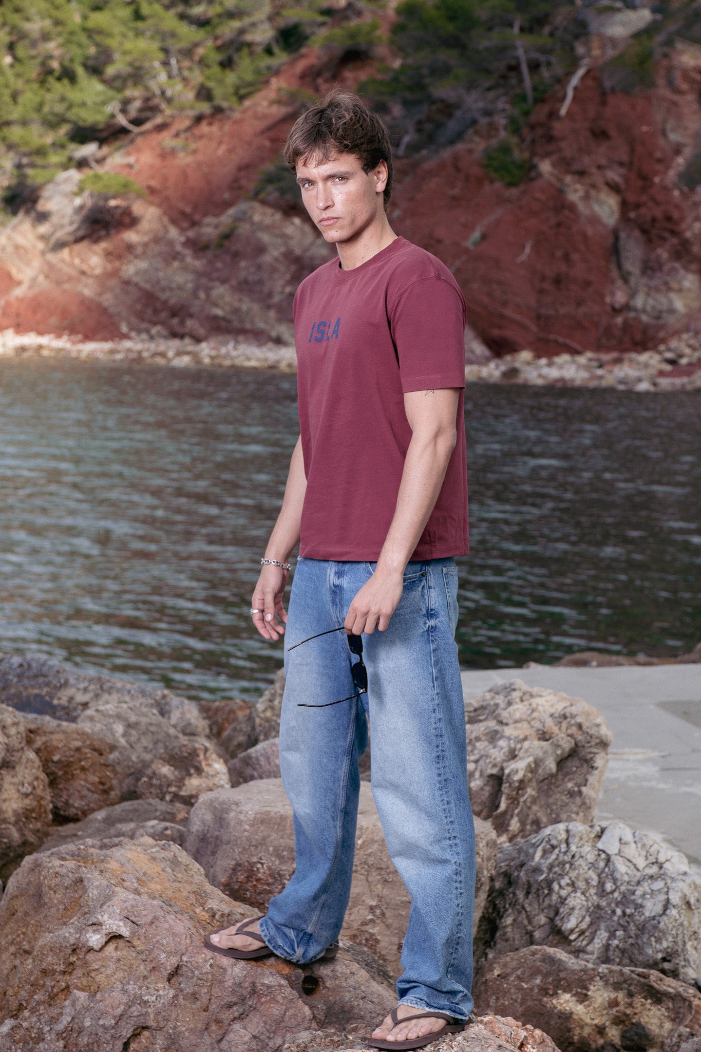 Man standing on rocks by a body of water with a scenic background