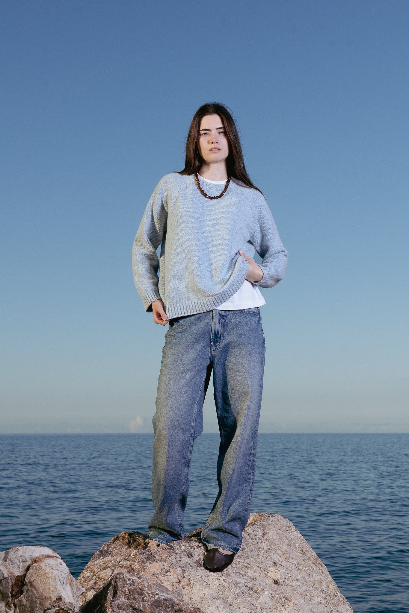 Person standing on a rock by the ocean with a clear blue sky