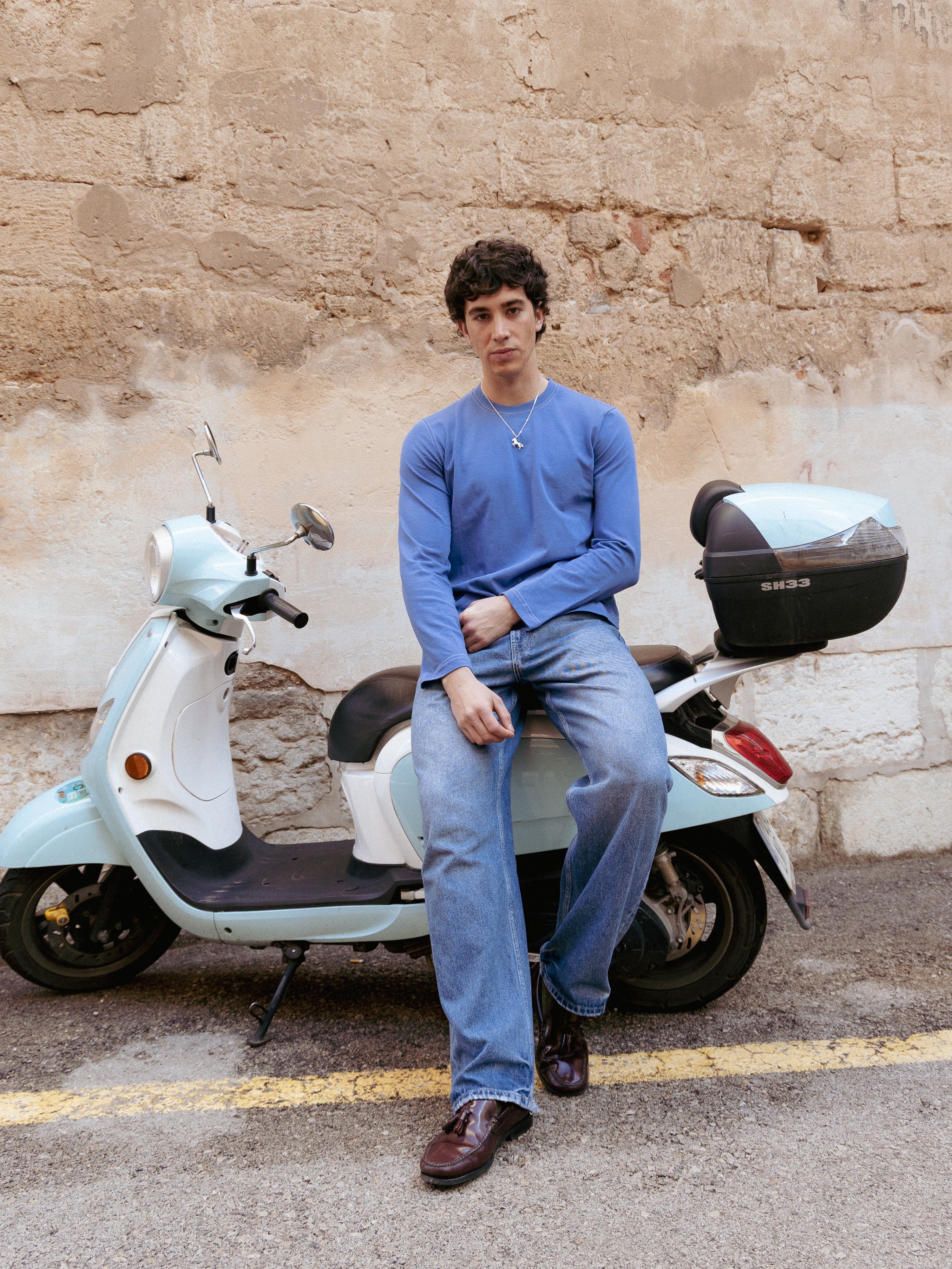 Person sitting on a scooter against a textured wall.