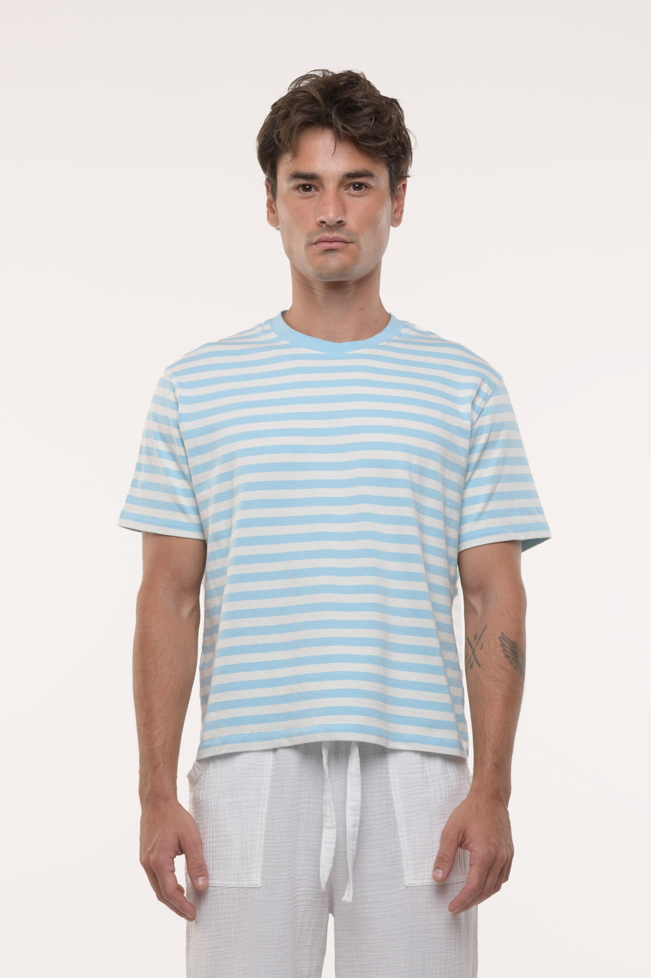 Man wearing a light blue and white striped t-shirt and white pants on a white background