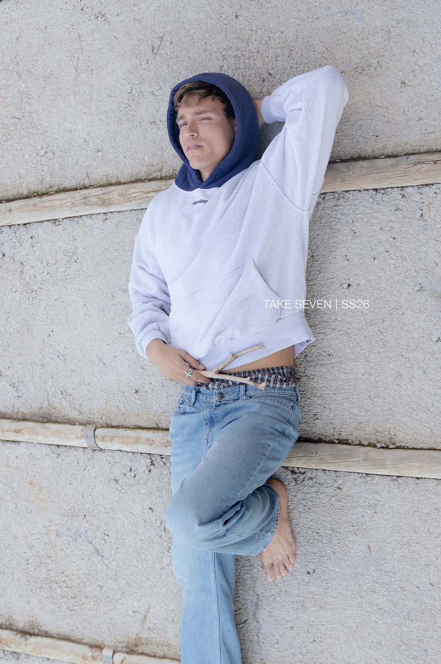 Person wearing a white hoodie and blue jeans leaning against a textured wall.