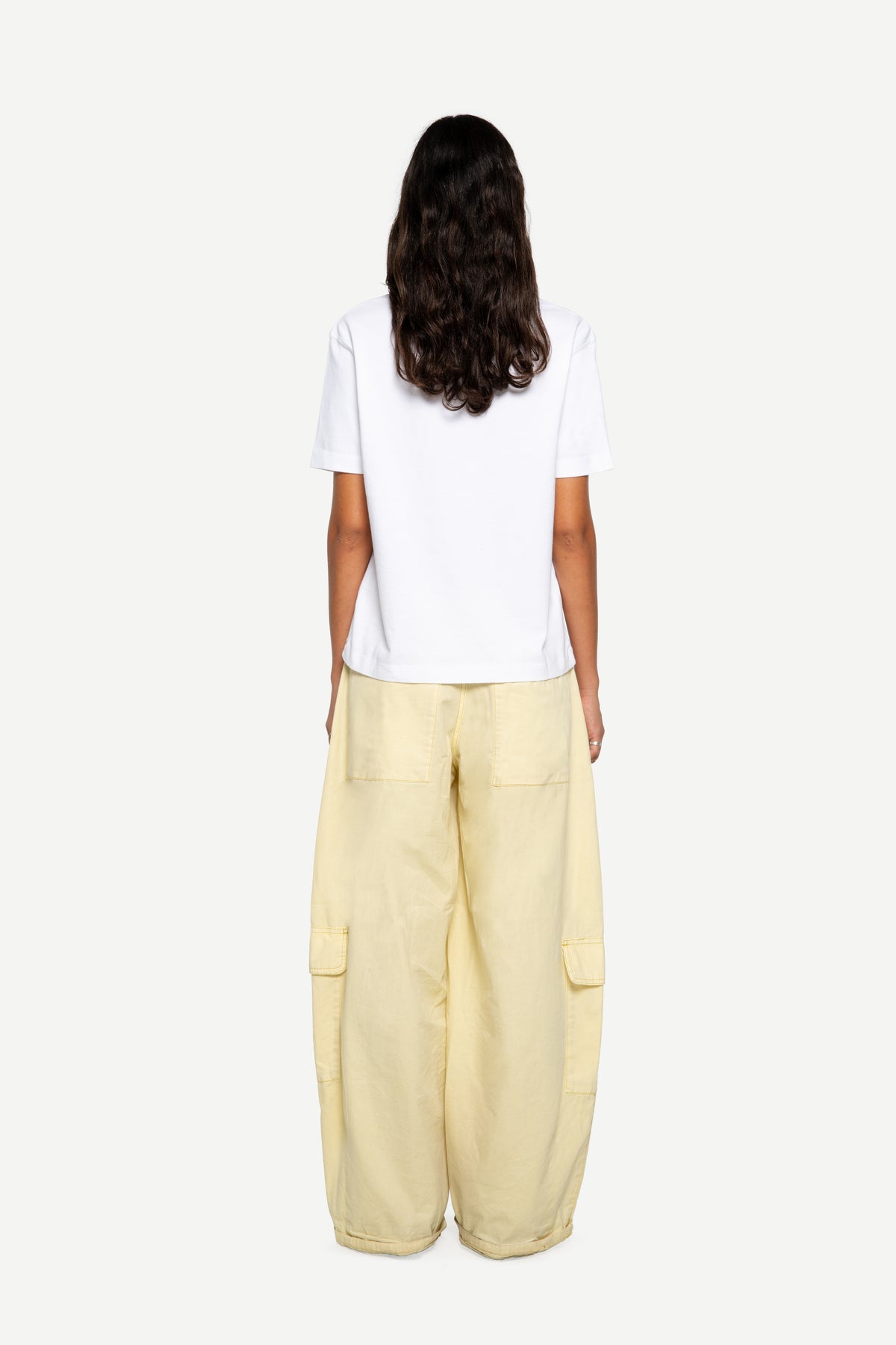 A model shown from the back wearing a white short-sleeve t-shirt and light yellow wide-leg cargo pants against a plain light gray background.
