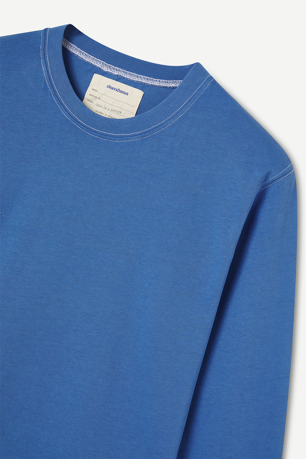 Blue long-sleeve shirt with a brand label  and contrast stichings on a light gray background