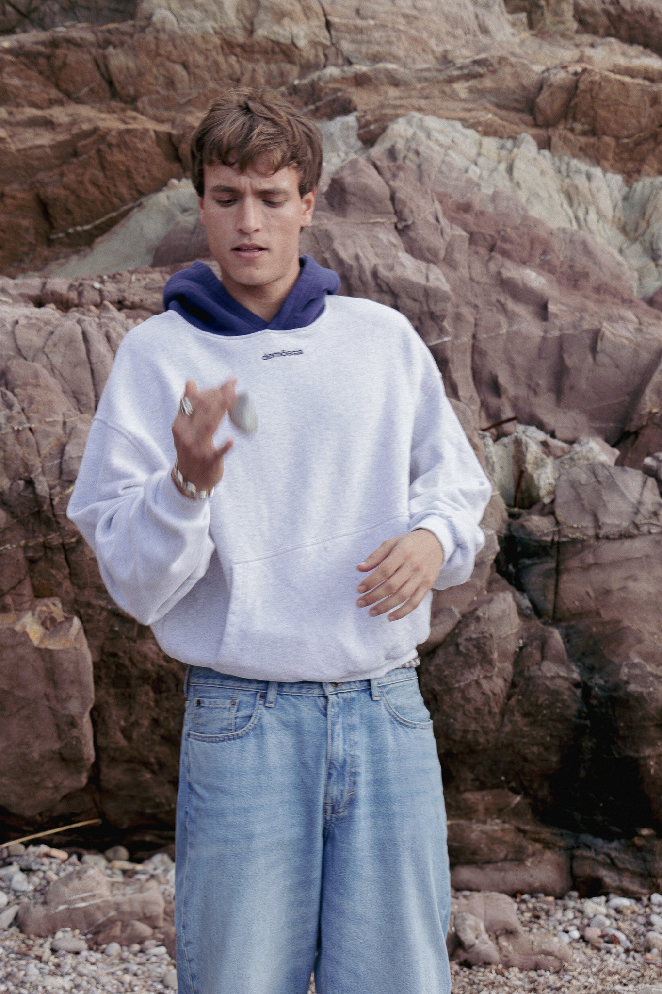 Person wearing a white sweatshirt and blue jeans standing against a rocky background