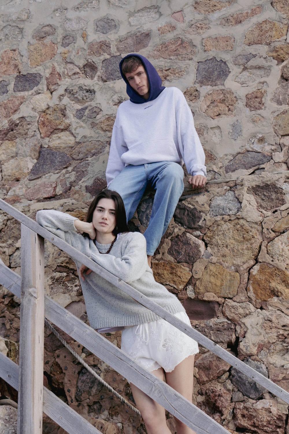 Two people sitting on a stone wall with a wooden railing.