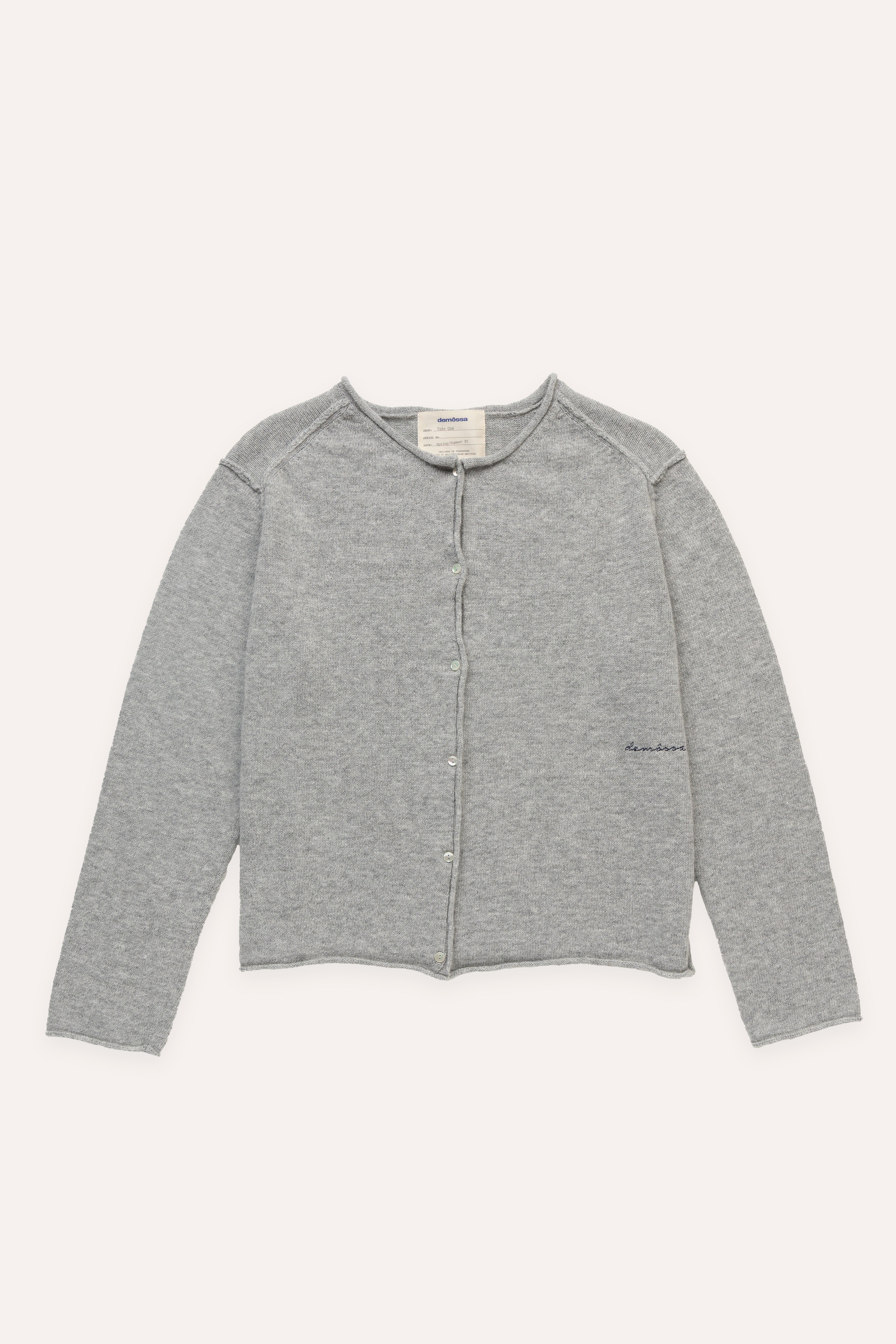 Flat lay of grey cardigan with button closure, raw-cut edges and subtle Demossa embroidery on the front left