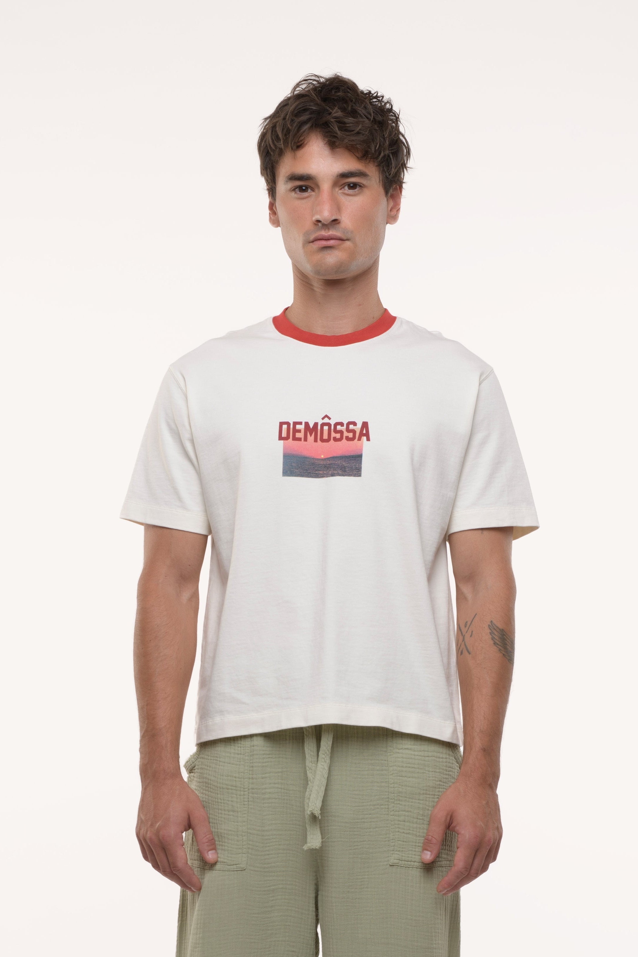 Man wearing a white t-shirt with a logo and light green pants on a white background