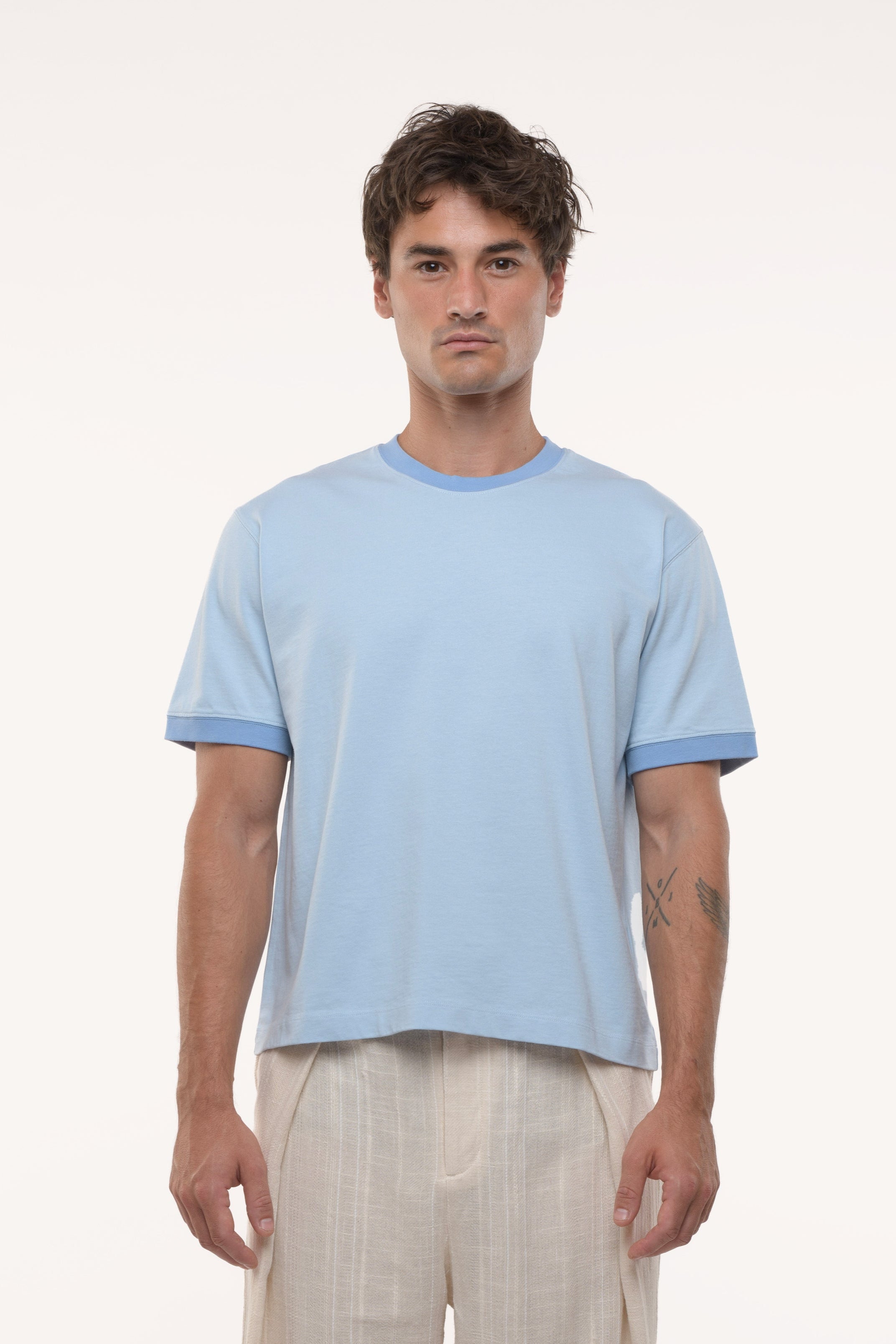 Man wearing a light blue t-shirt and beige pants on a white background