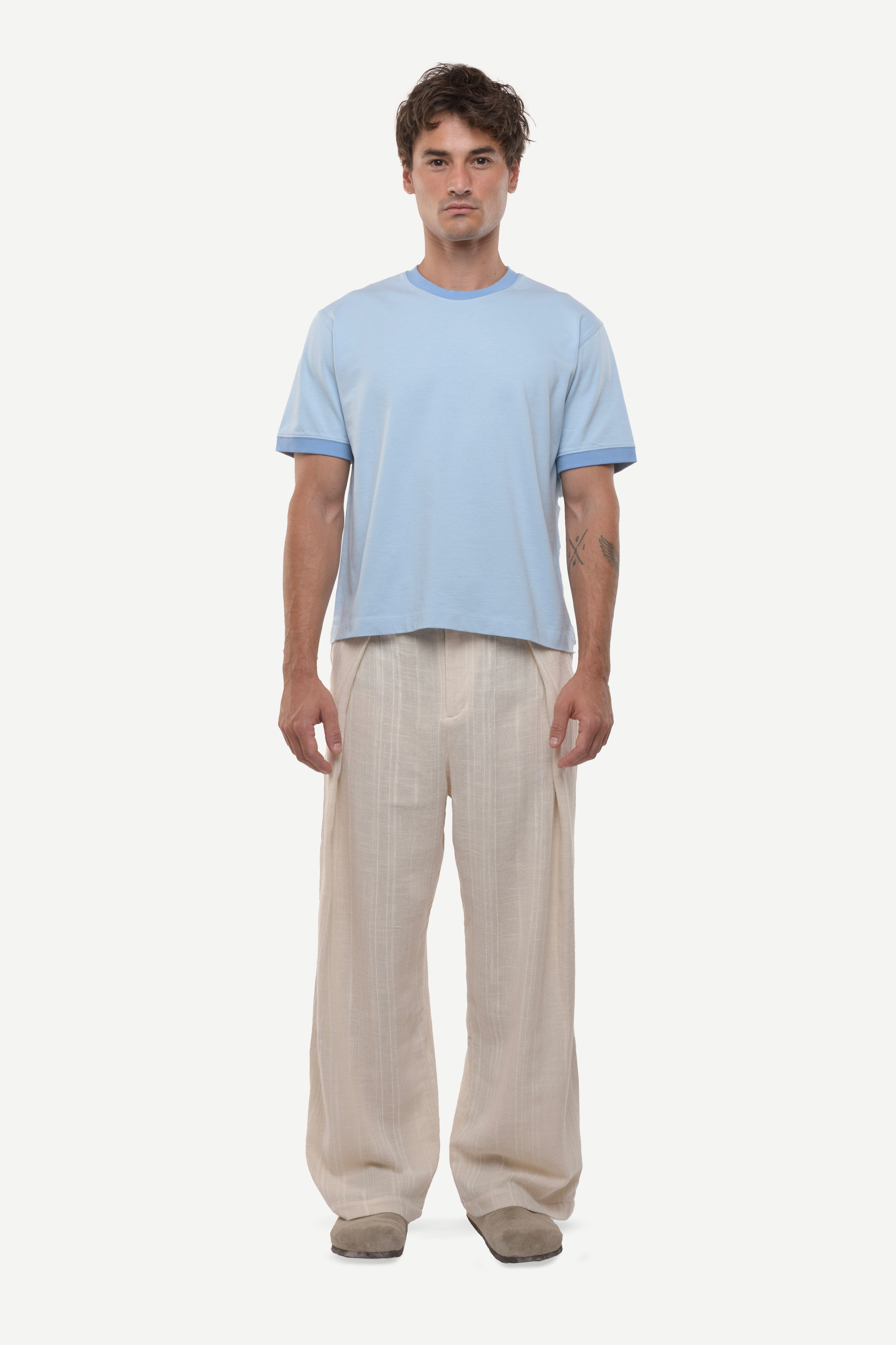 Man wearing a light blue t-shirt with contras ribs and beige pants on a white background