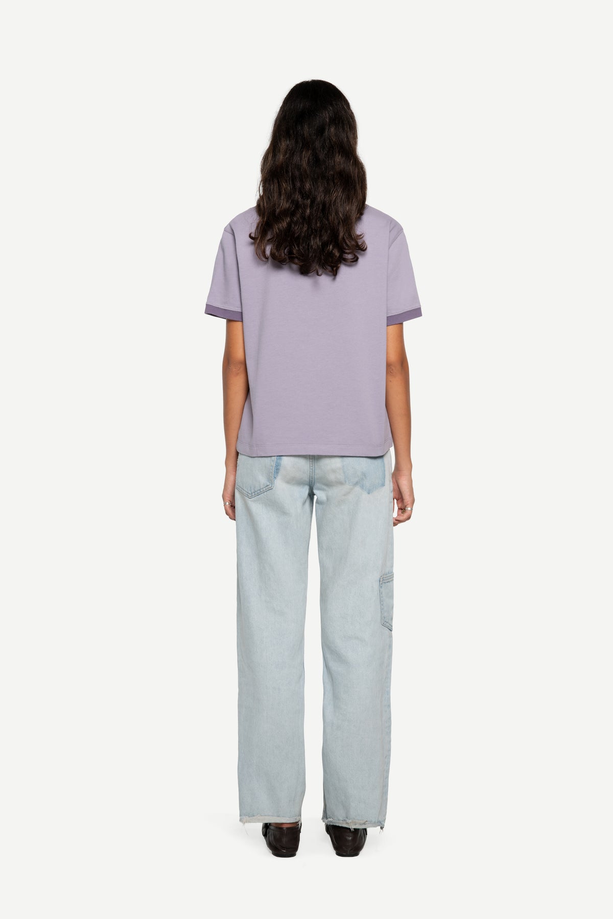A model viewed from the back wearing a lavender short-sleeve t-shirt and light-wash wide-leg jeans against a plain white background.