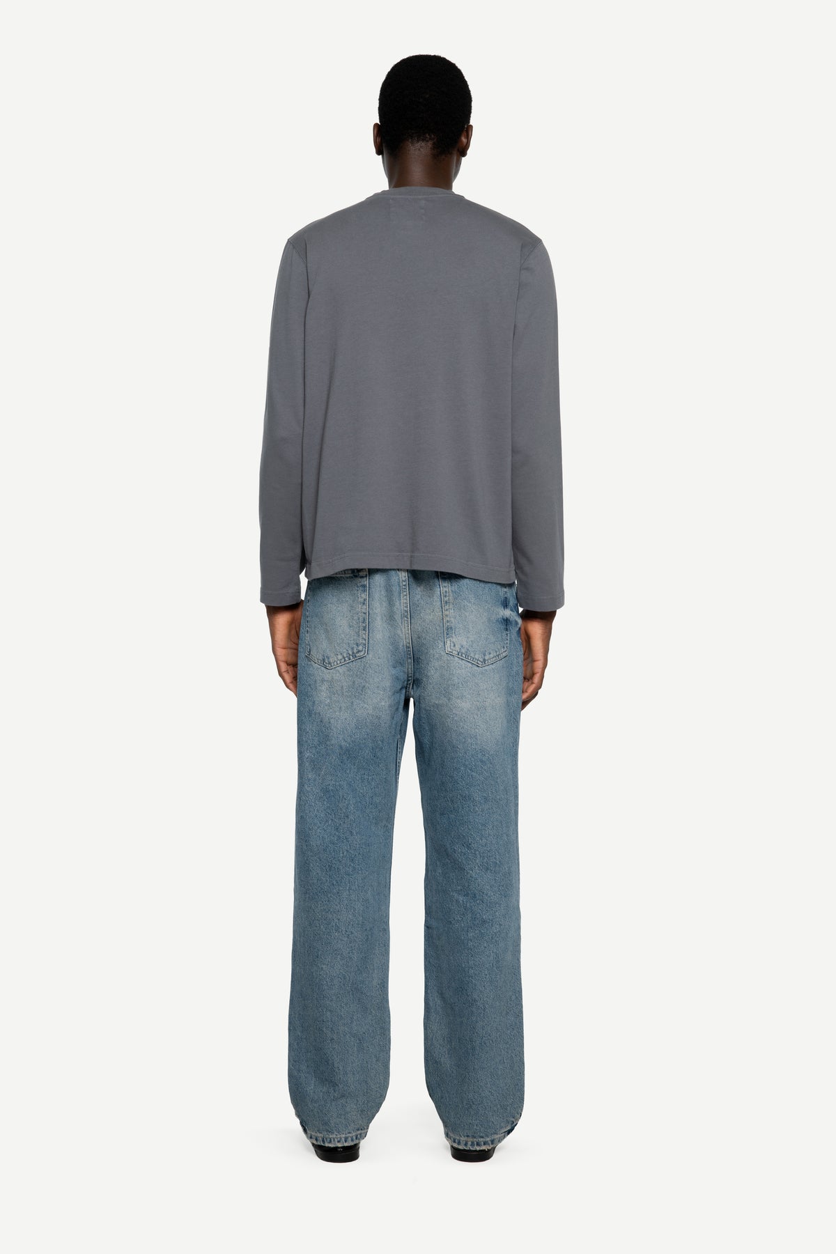 A model shown from the back wearing a gray long-sleeve top and light blue wide-leg jeans against a plain light gray background.