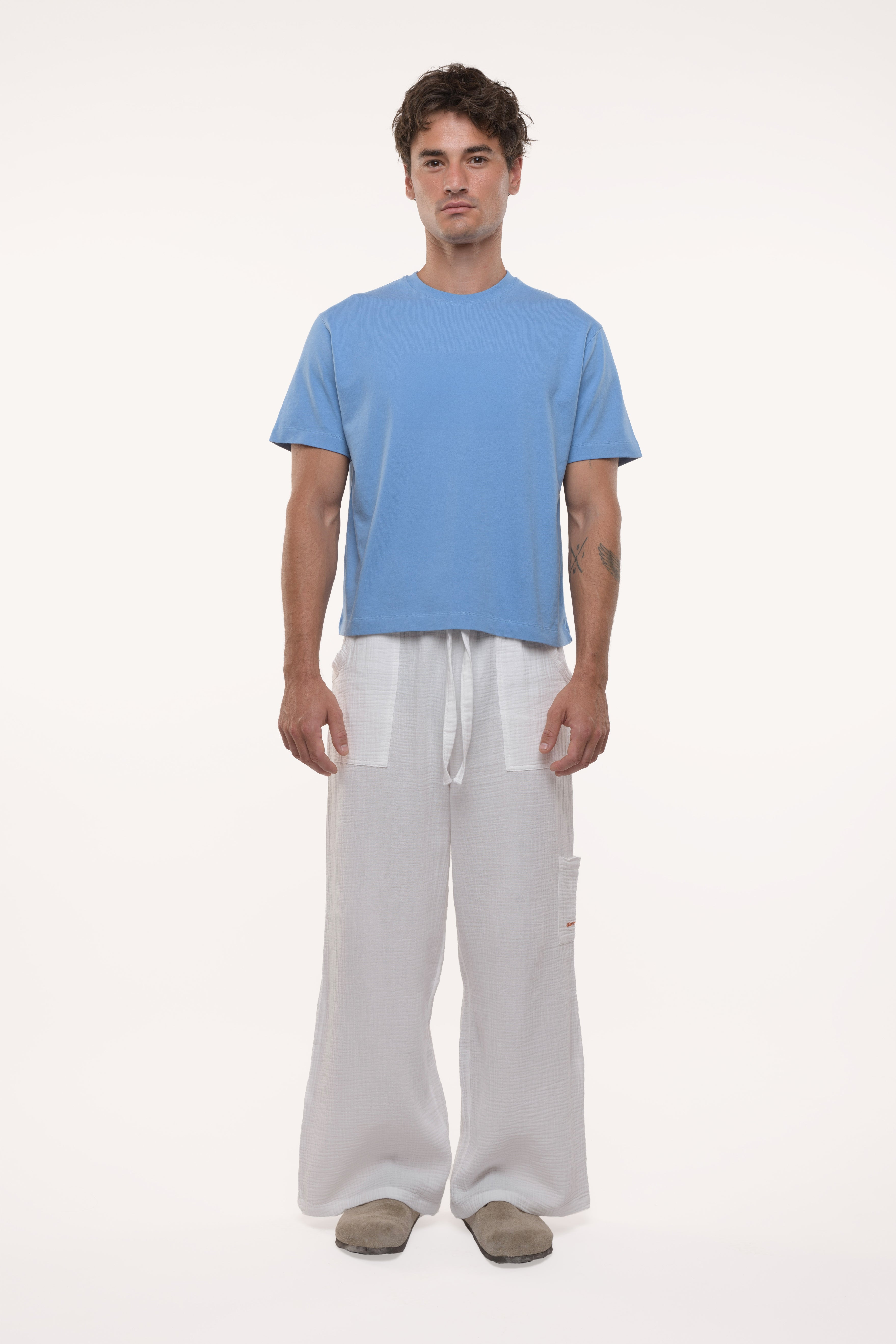Man wearing a light blue t-shirt and white 
cotton pants on a white background