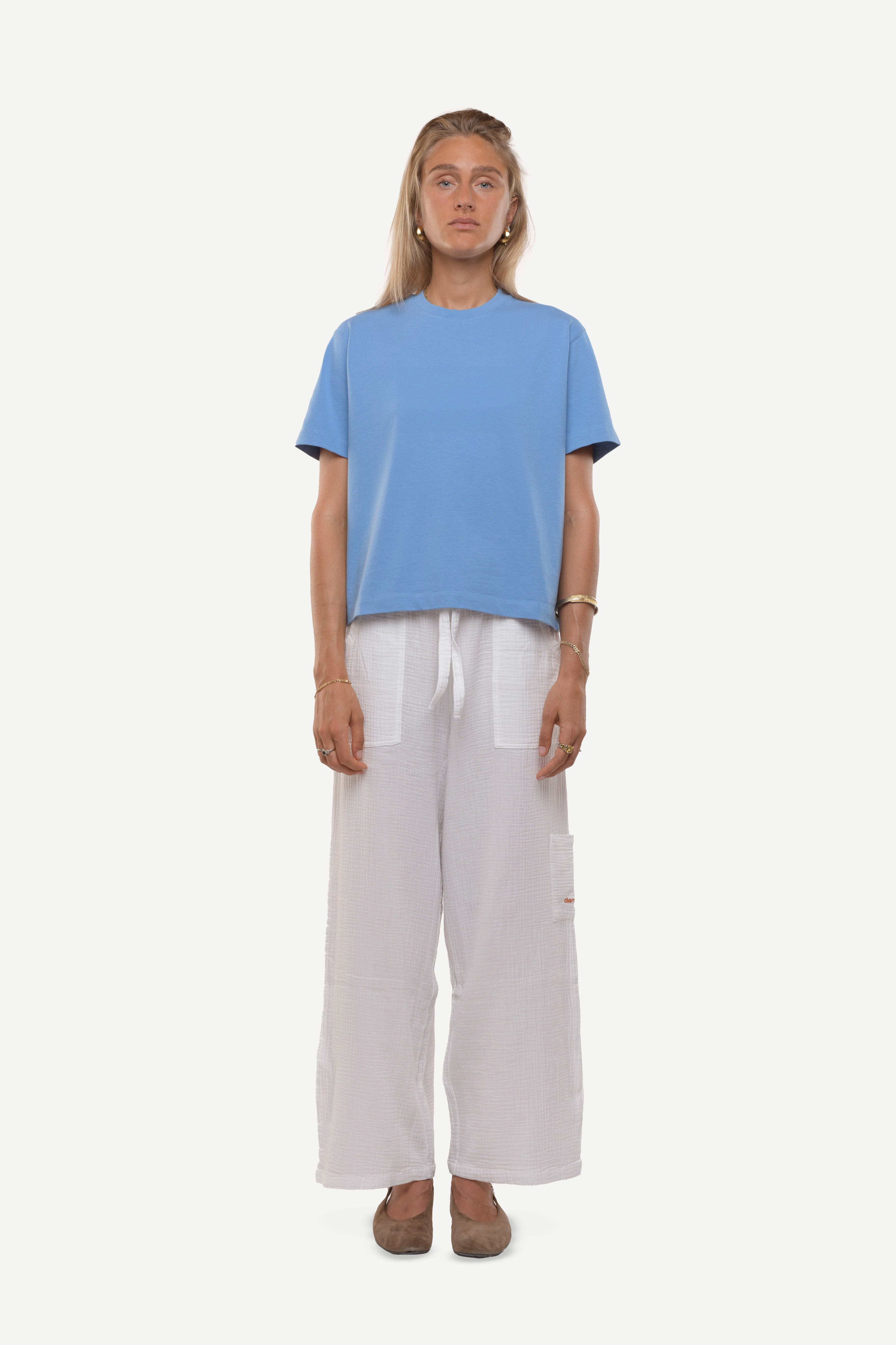 Woman wearing a blue cotton t-shirt and white cotton pants on a white background