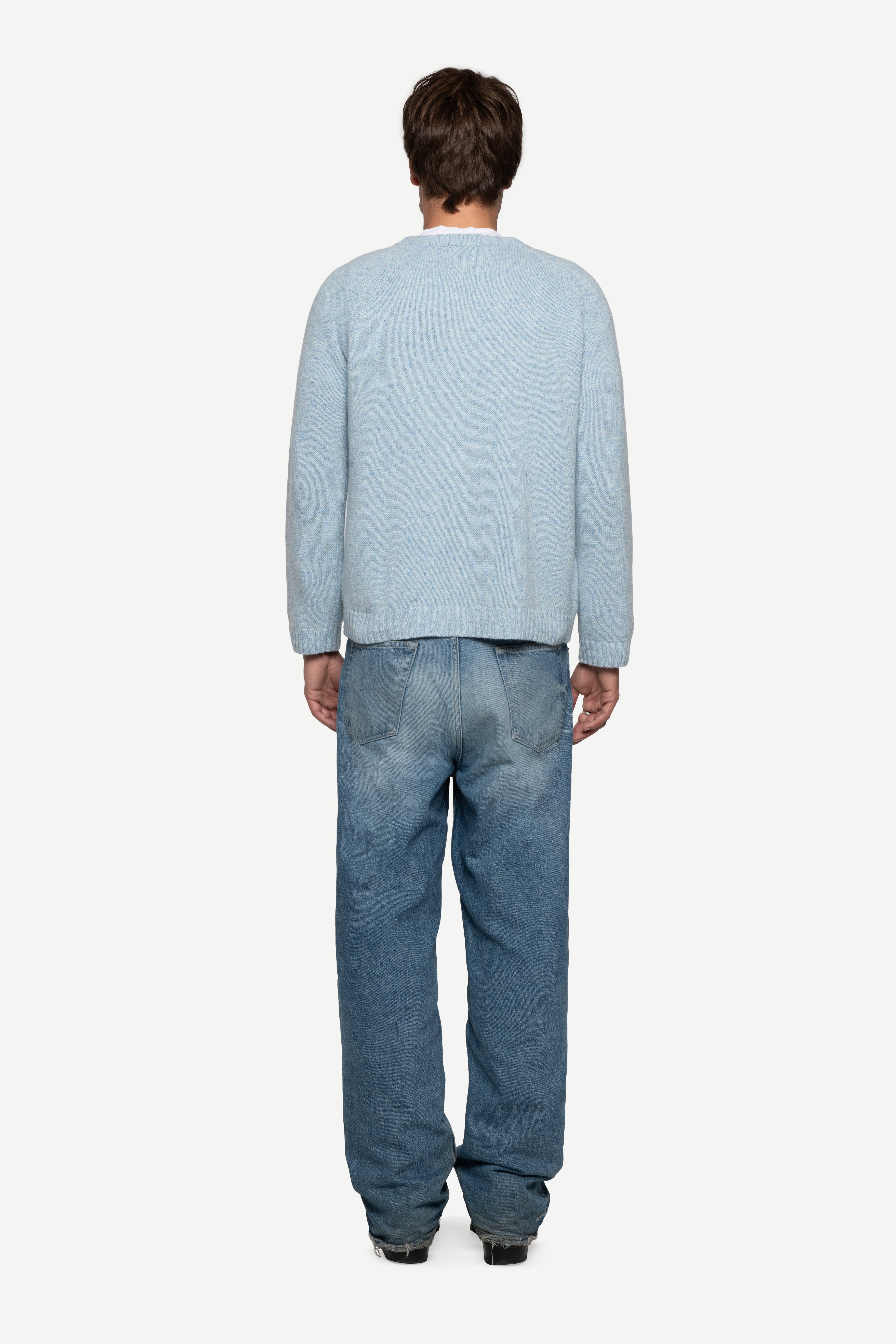 back view of man wearing a blue sweater made from a soft blend of wool and silk with blue short jeans on a white background