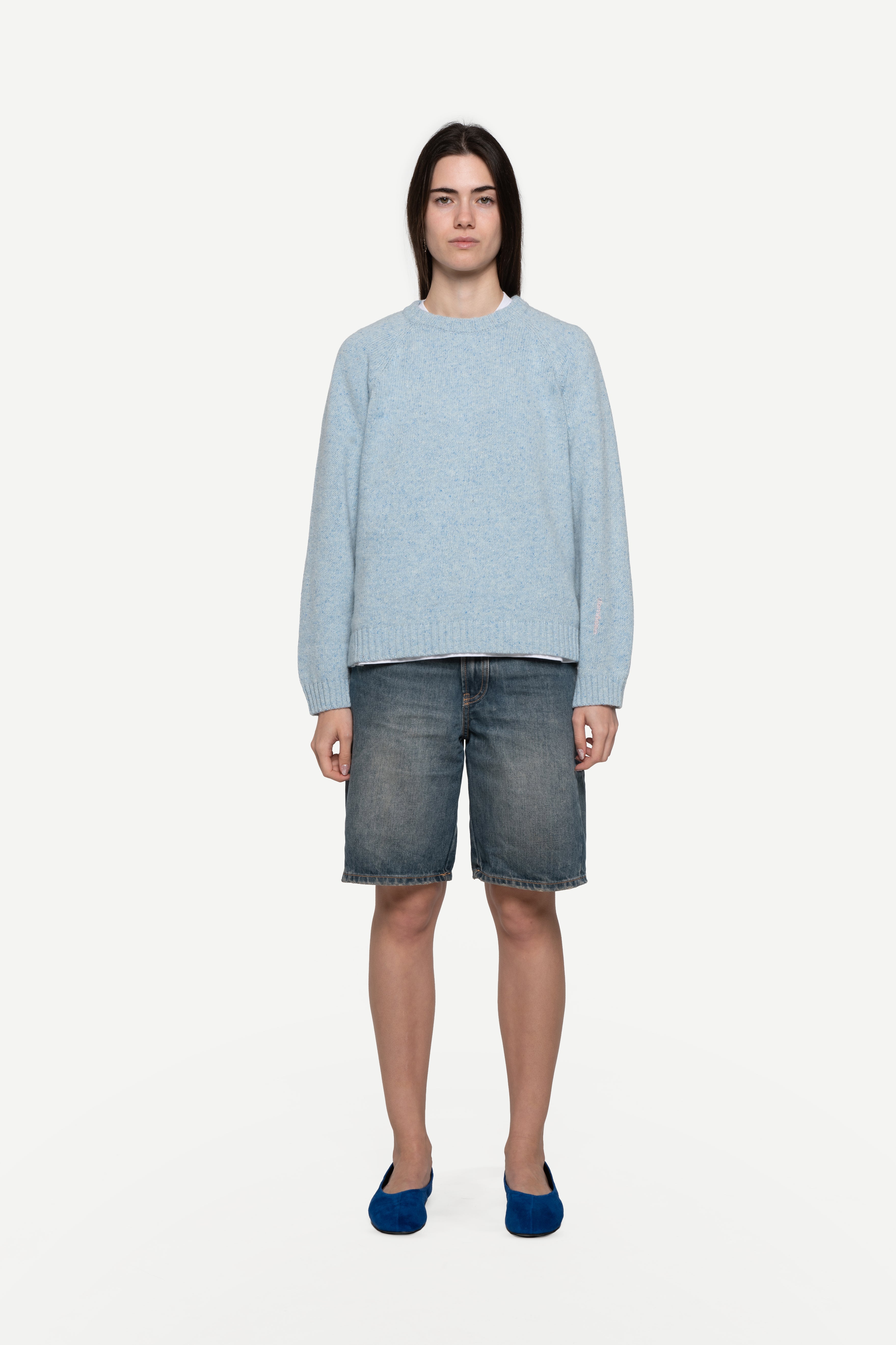 front view of woman wearing a blue sweater made from a soft blend of wool and silk with blue short jeans on a white background