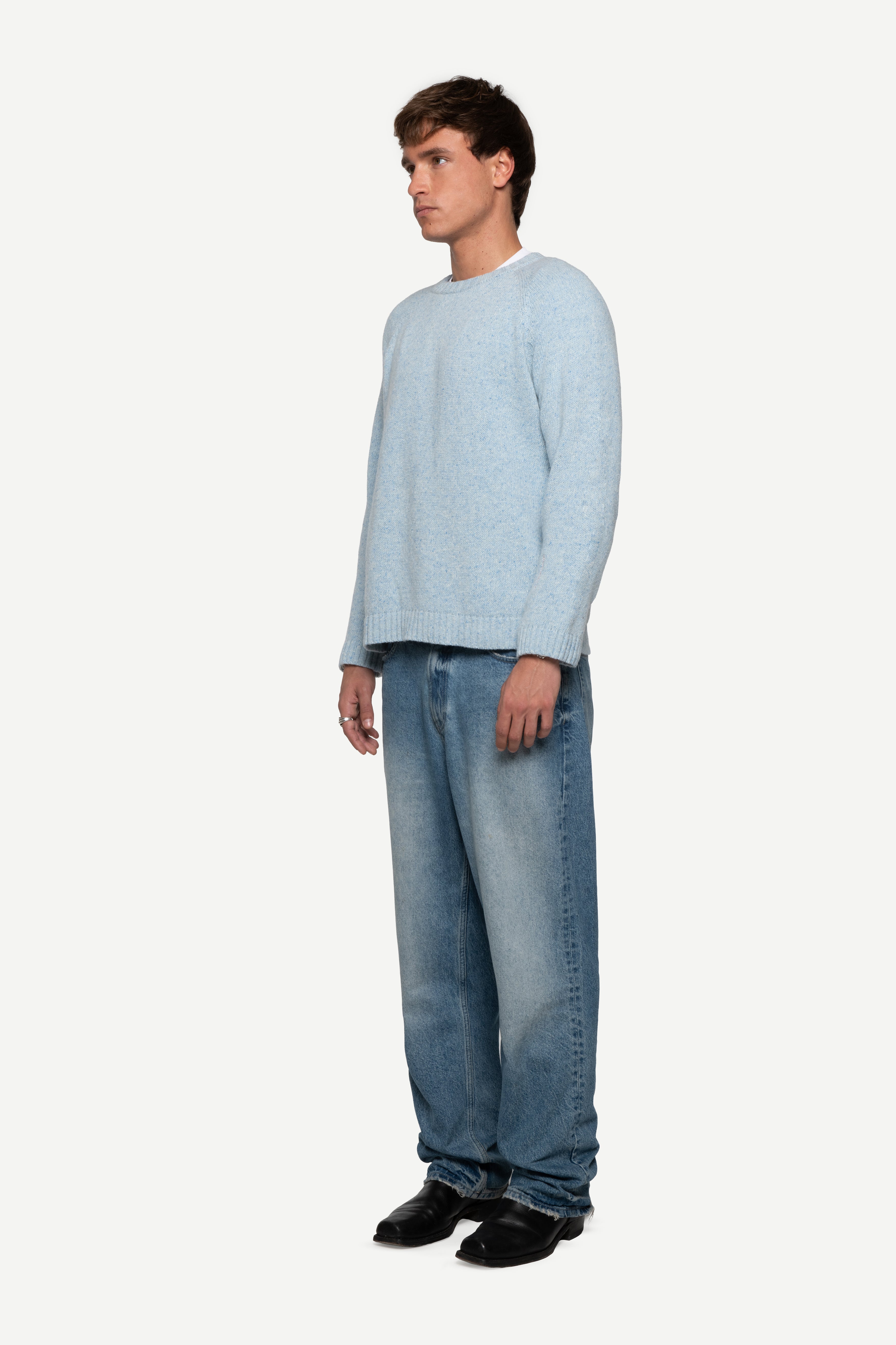 side view of man wearing a blue sweater made from a soft blend of wool and silk with blue short jeans on a white background