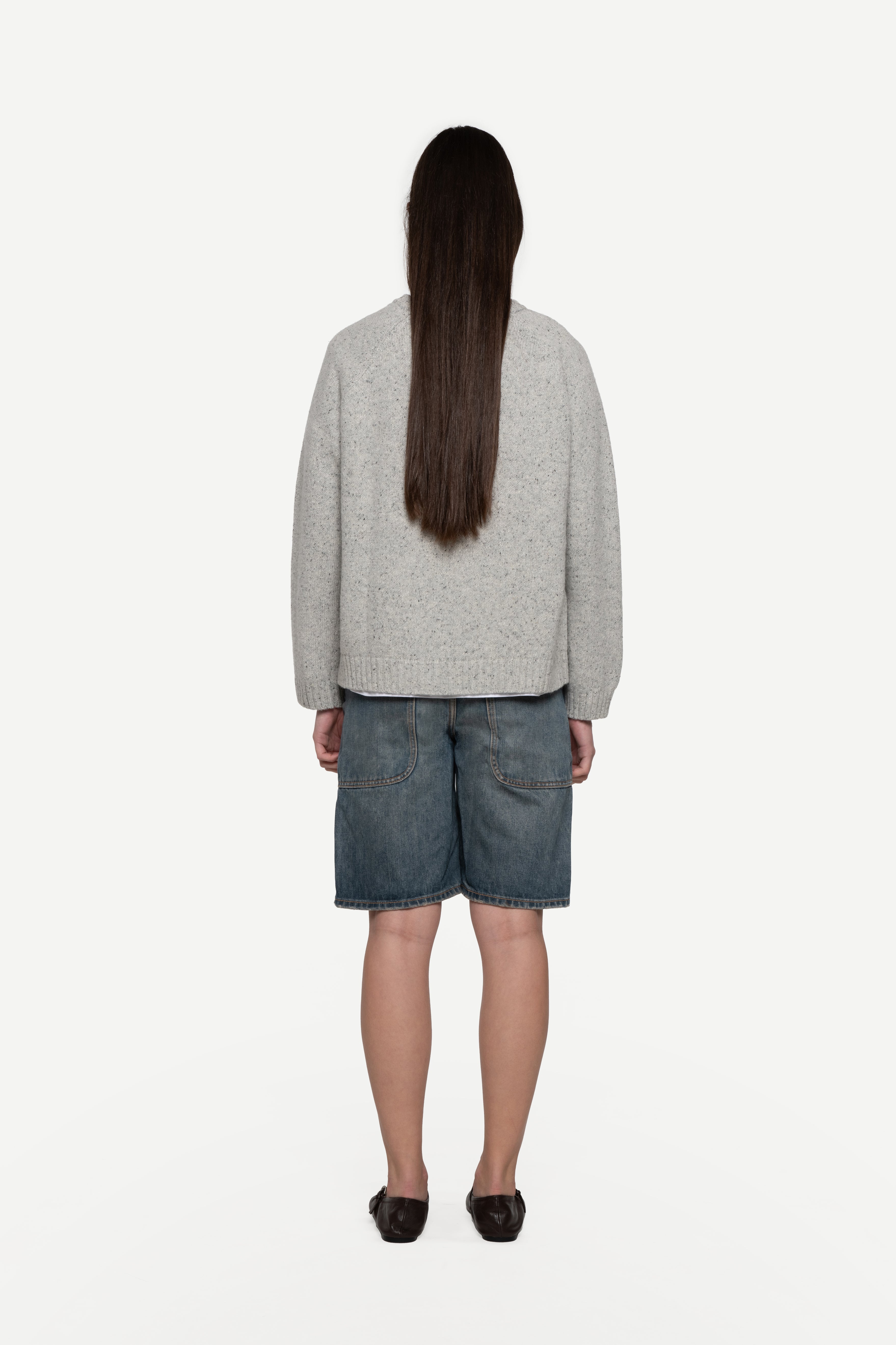 back view of woman wearing a grey sweater made from a soft blend of wool and silk with blue short jeans on a white background