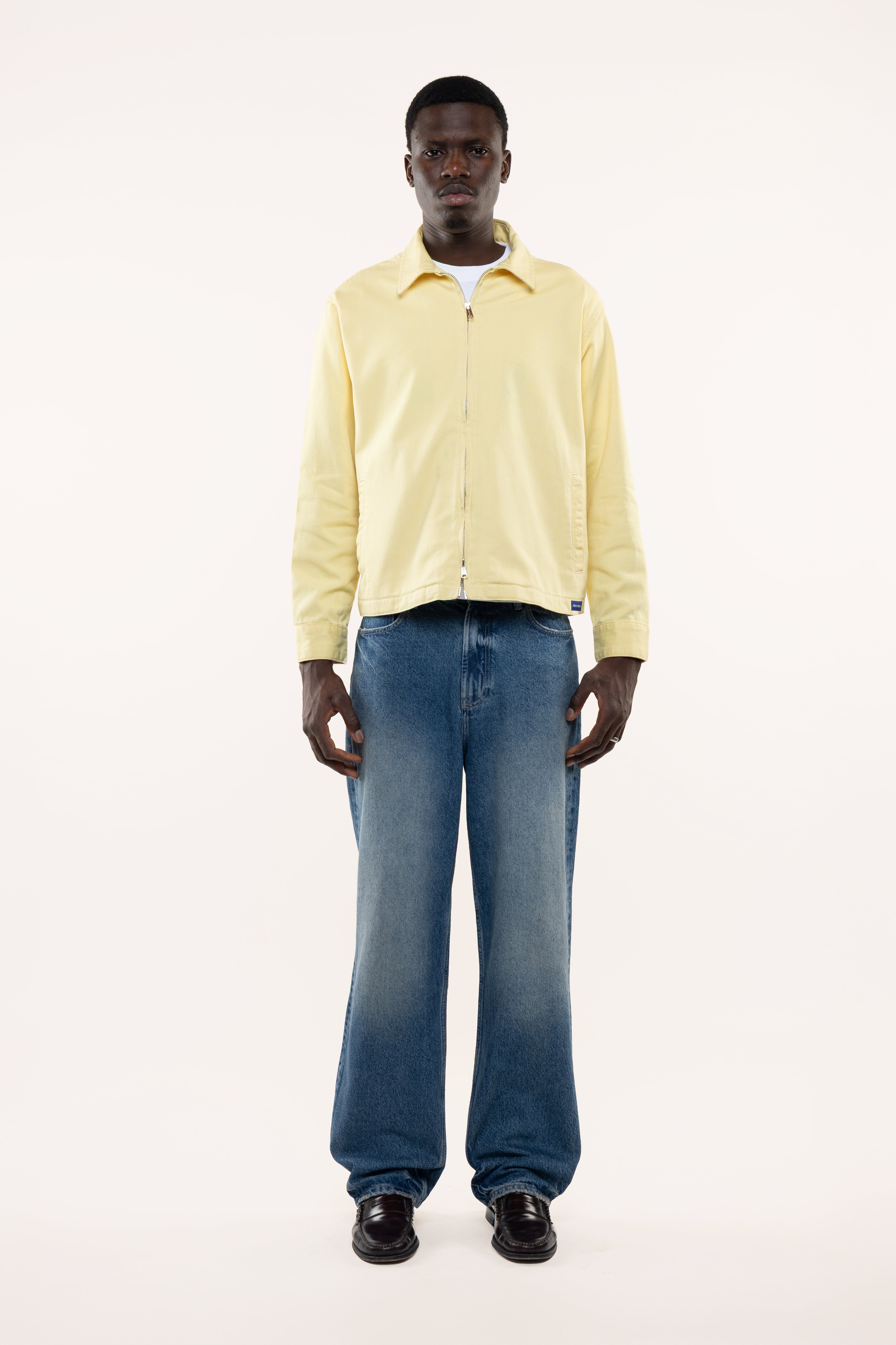 Man wearing a light yellow shirt and blue jeans on a white background