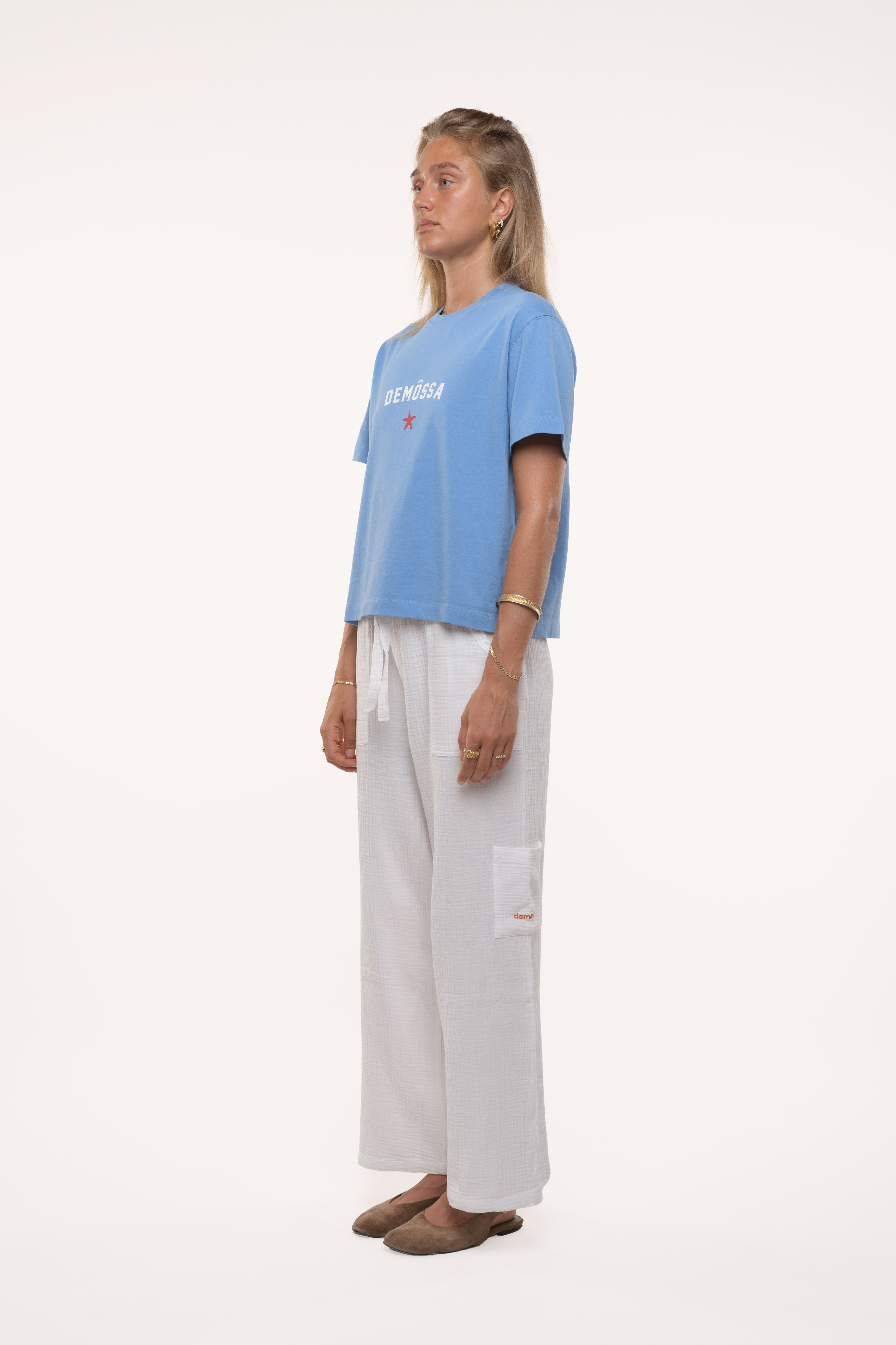 Side profile of a girl wearing a light blue t-shirt and white pants on a white background