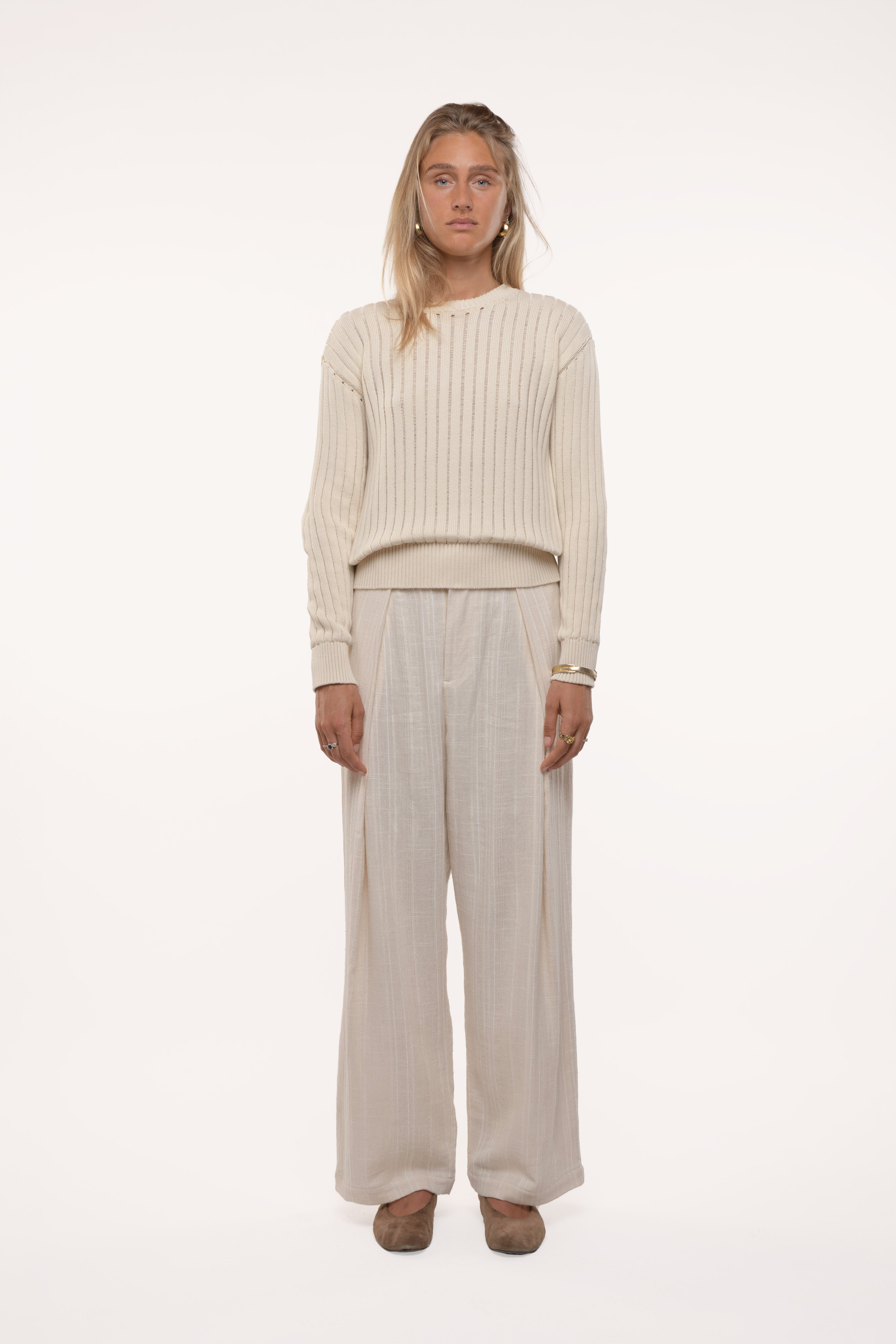 Woman wearing a beige ribbed sweater and wide-leg pants on a white background