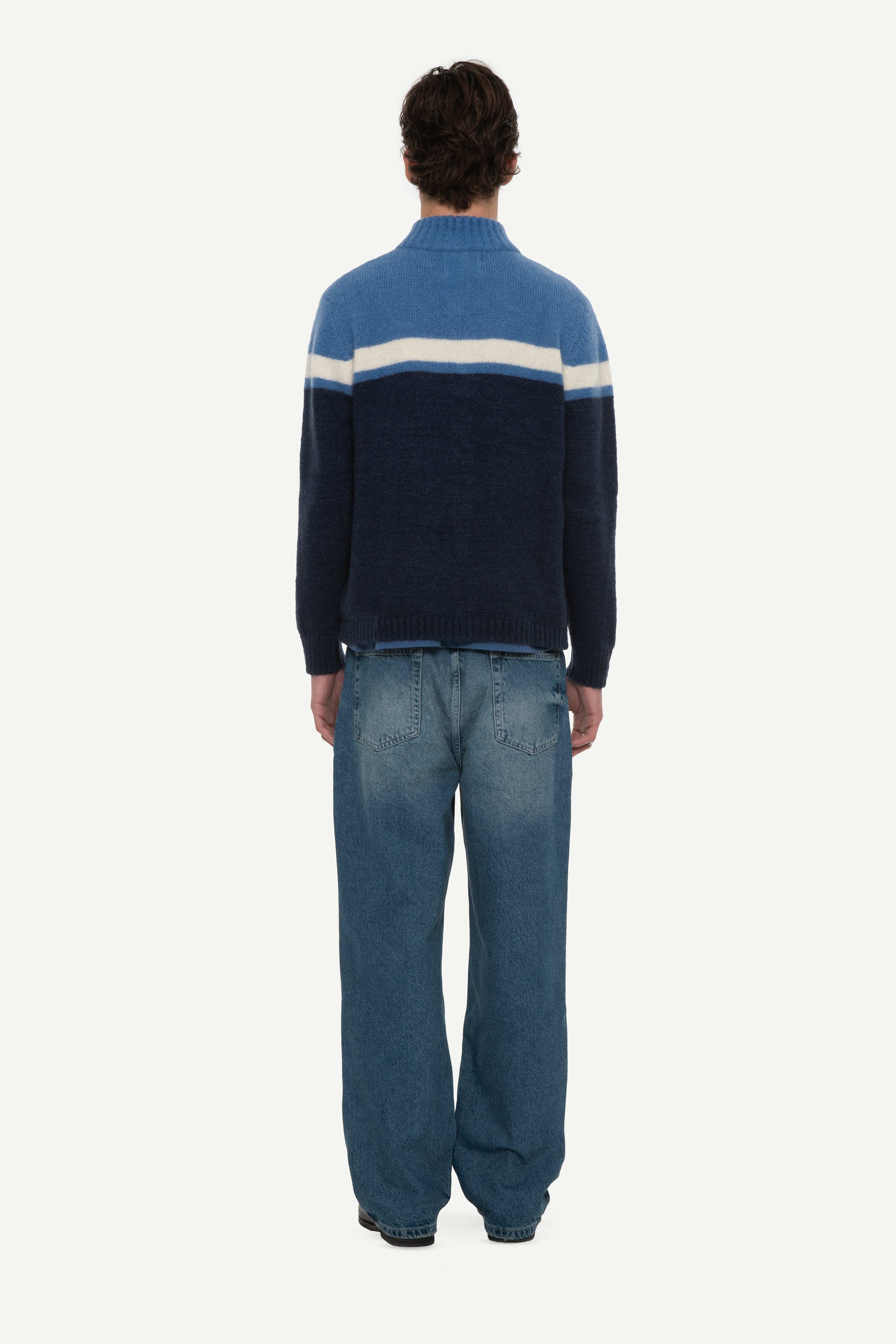 back view of man wearing a mohair zip cardigan with two shades of blue and white stripe at chest and blue jeans on a white background