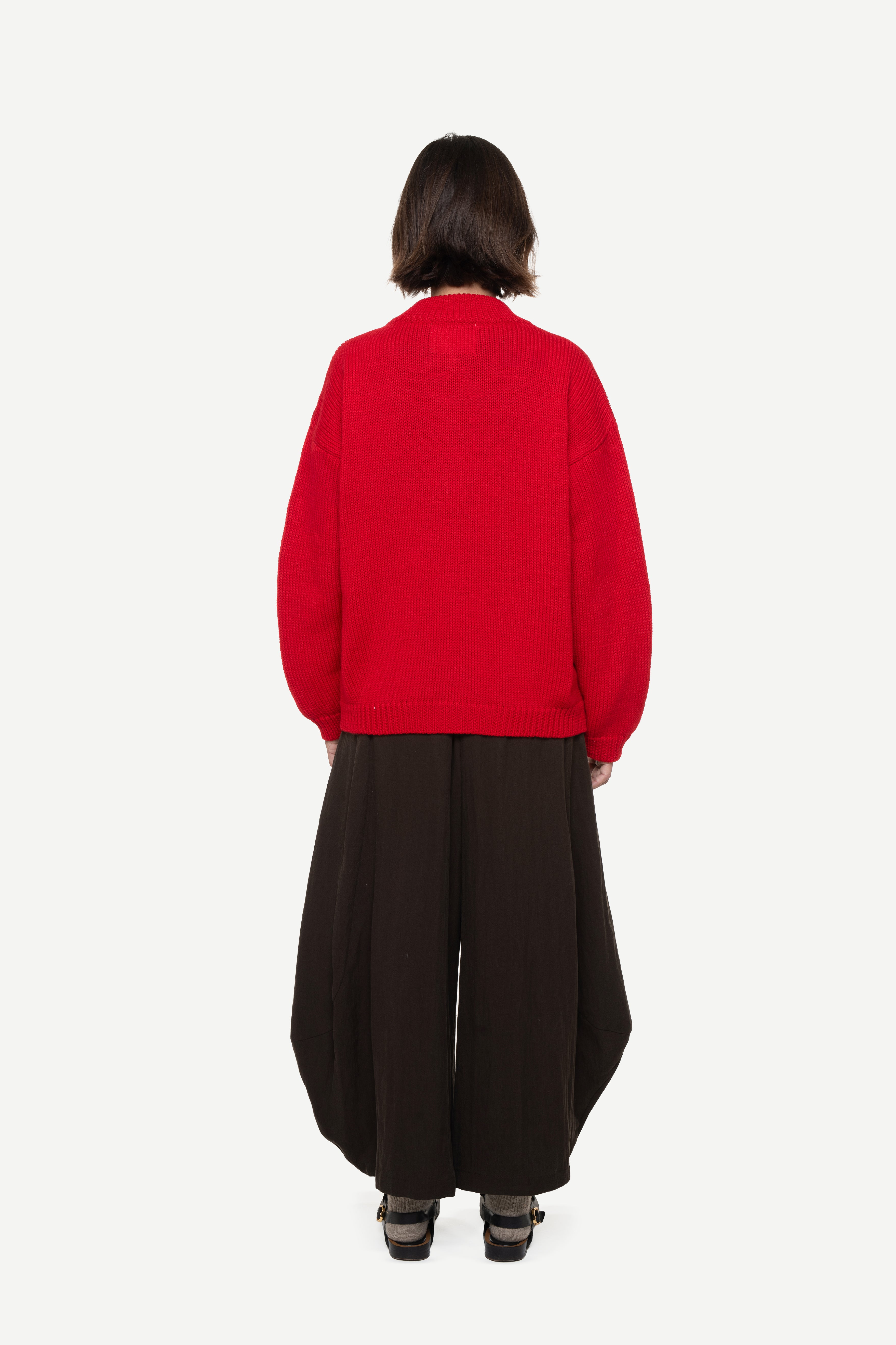 back view of a woman wearing a red cardigan and brown pants on a white background