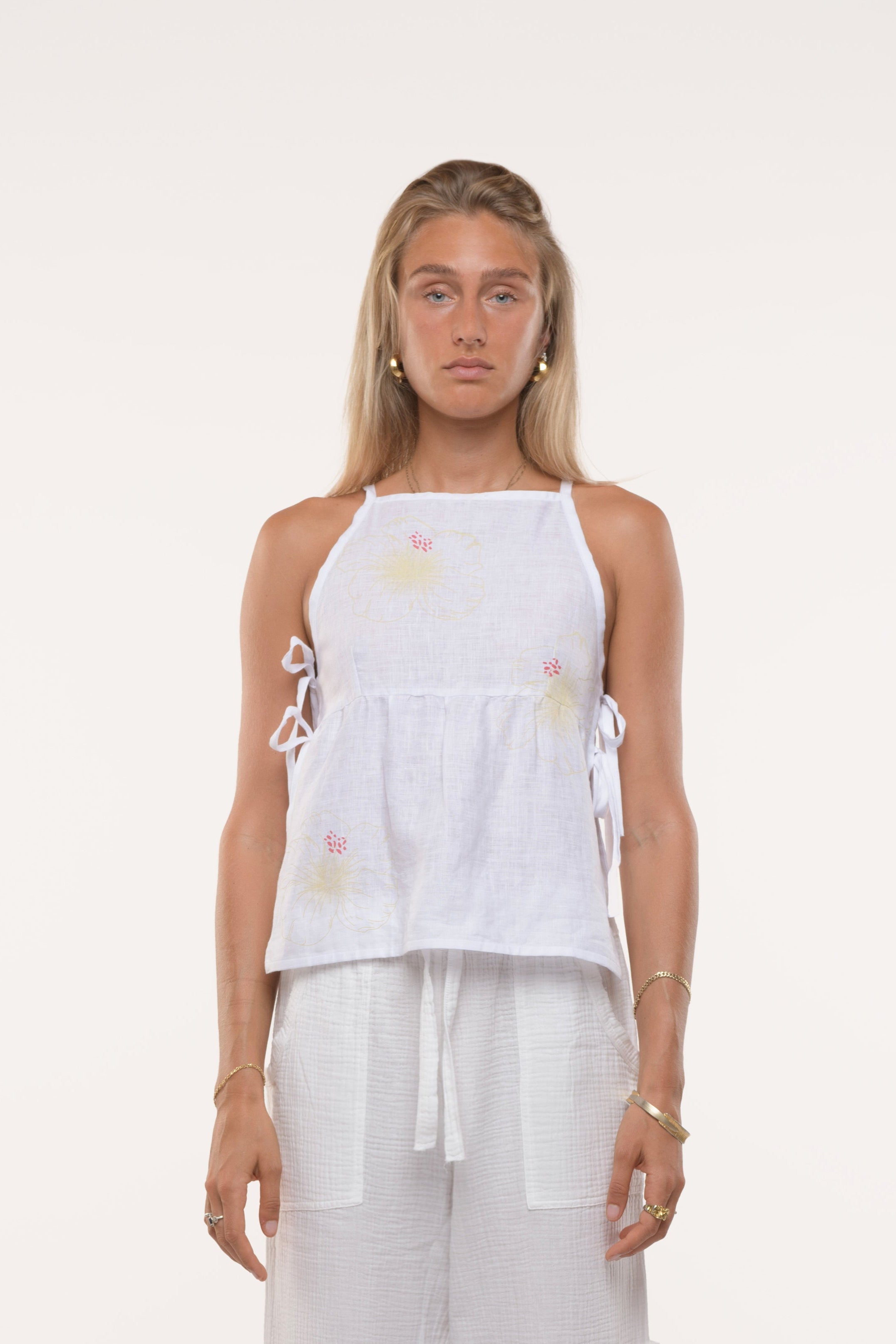 Woman wearing a white sleeveless top and wide-leg pants on a white background