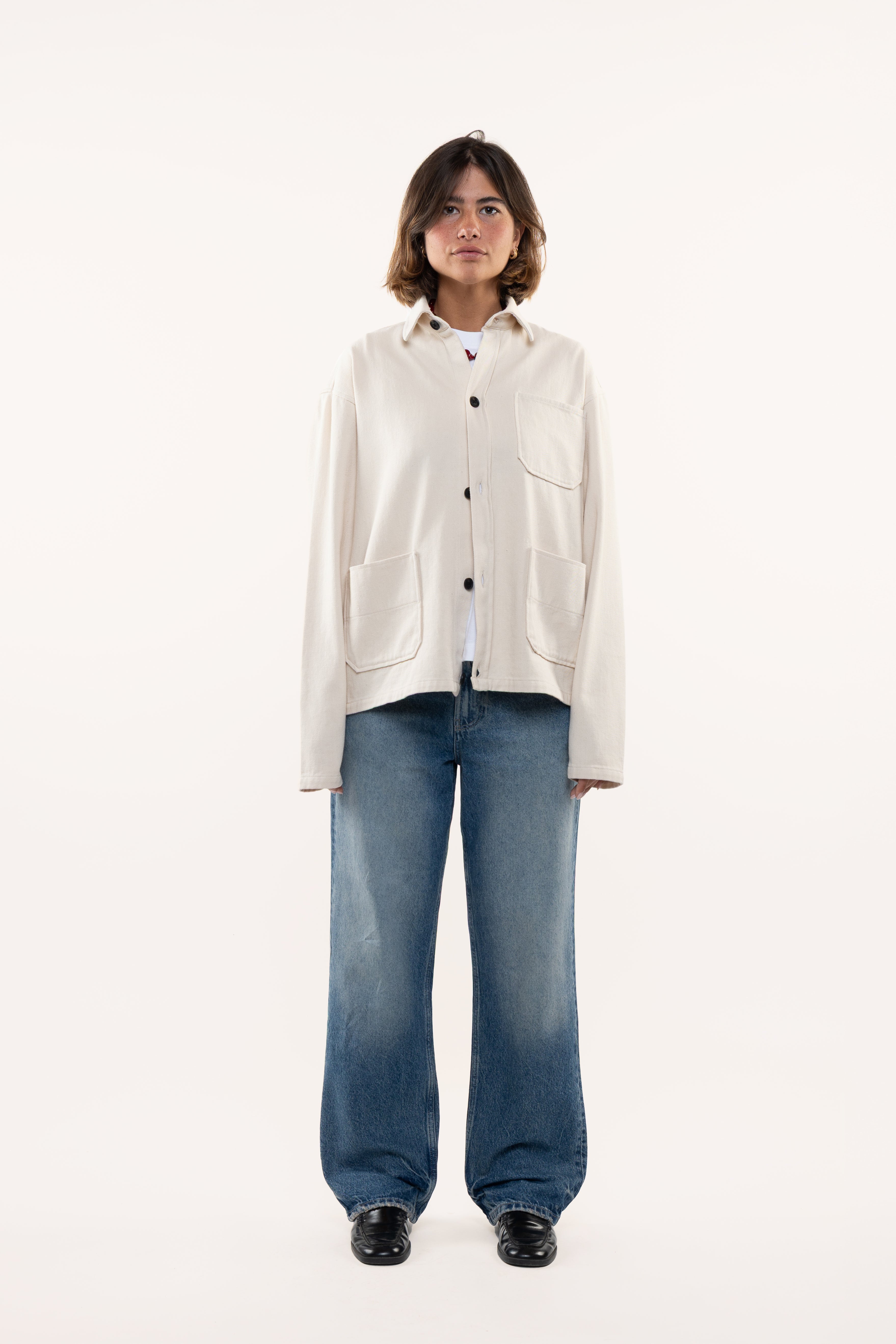 Woman wearing a cream overshirt and blue jeans on a white background