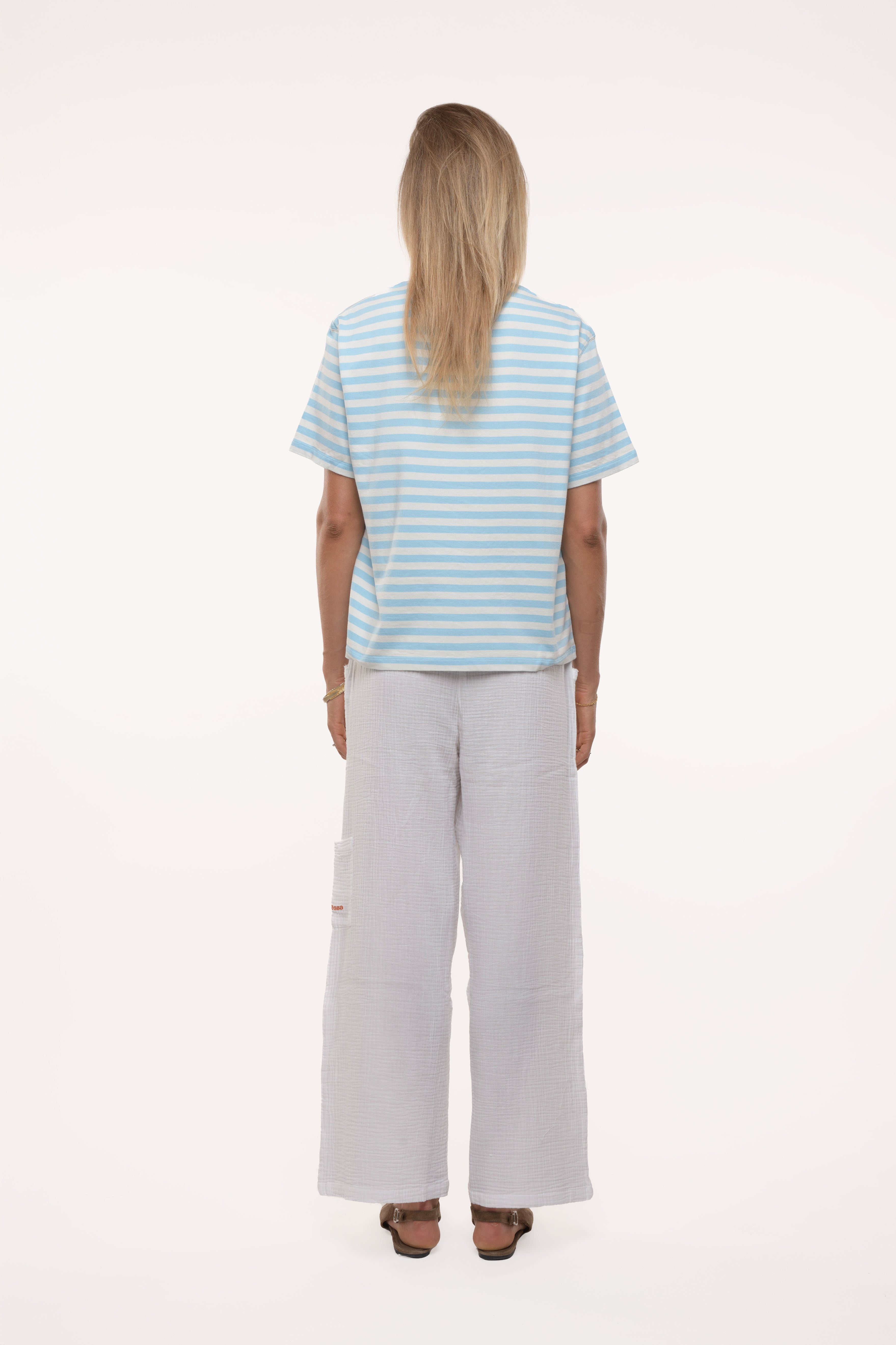 Back view of a woman wearing a striped shirt and light-colored pants on a white background