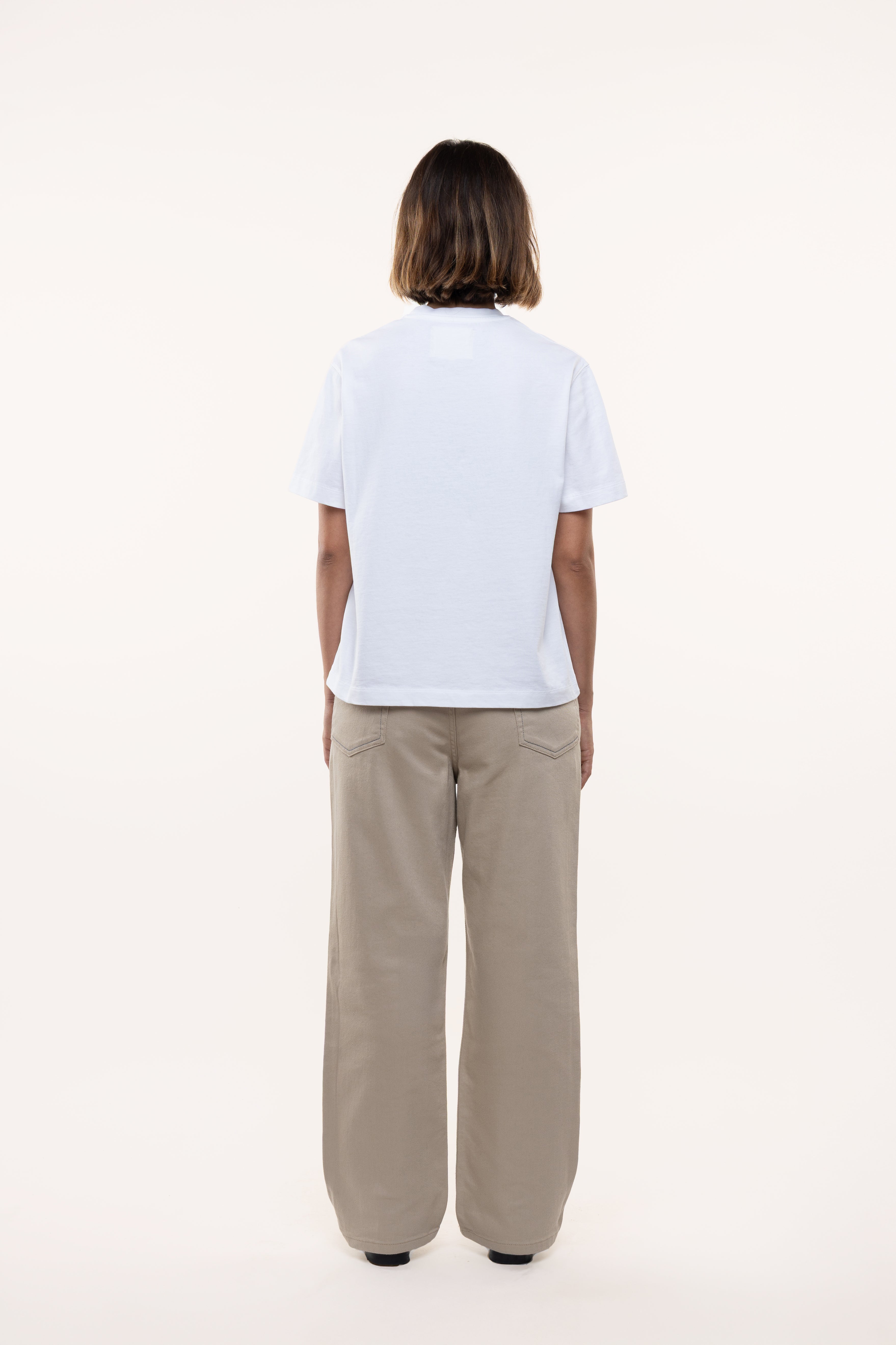 Back view of a woman wearing a light blue t-shirt and beige pants on a white background