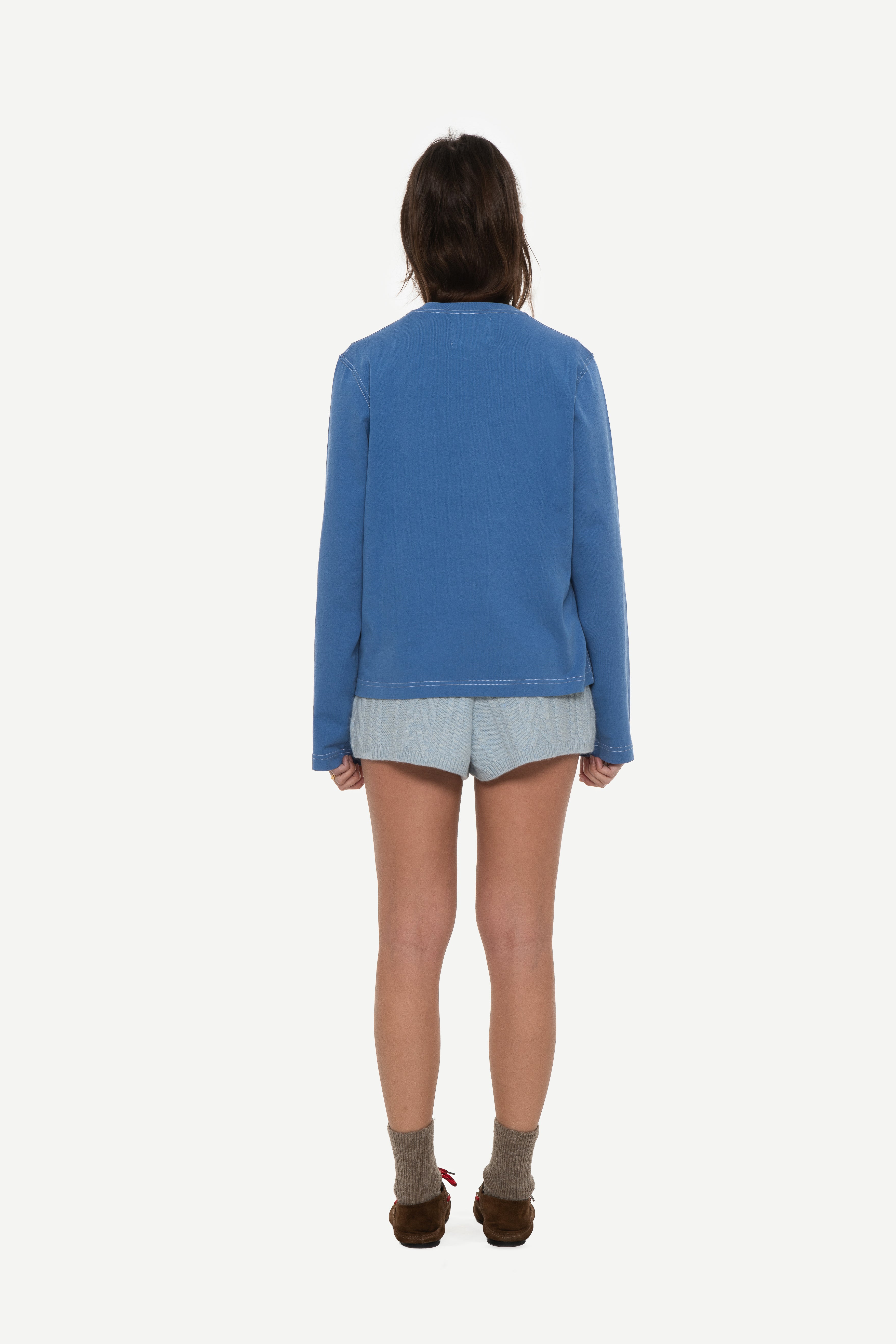 back view of woman wearing a blue long sleeve tee with contrast stitching and blue shorts on a white background