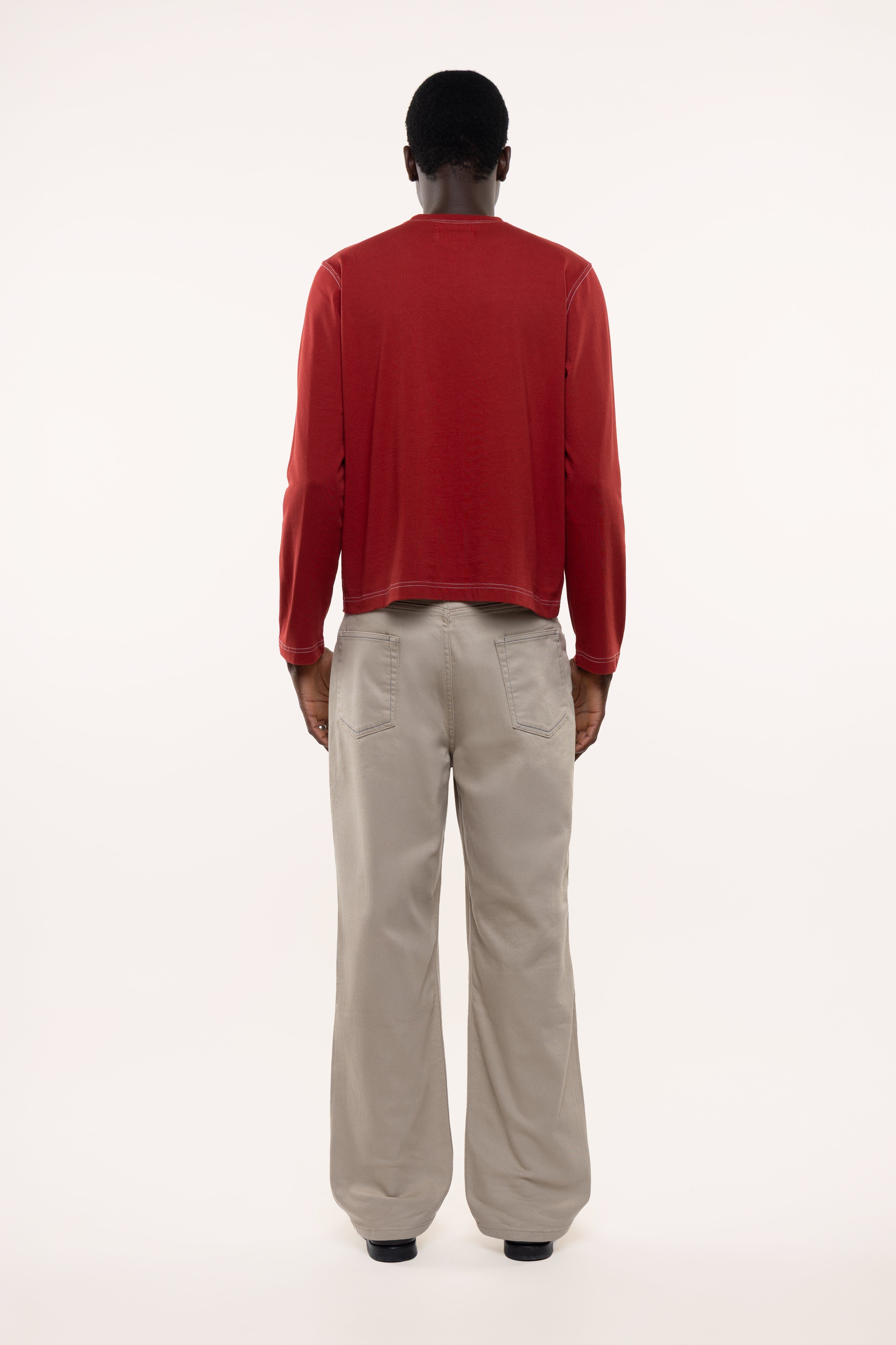 Back view of a man wearing a red longsleeve and beige pants on a white background
